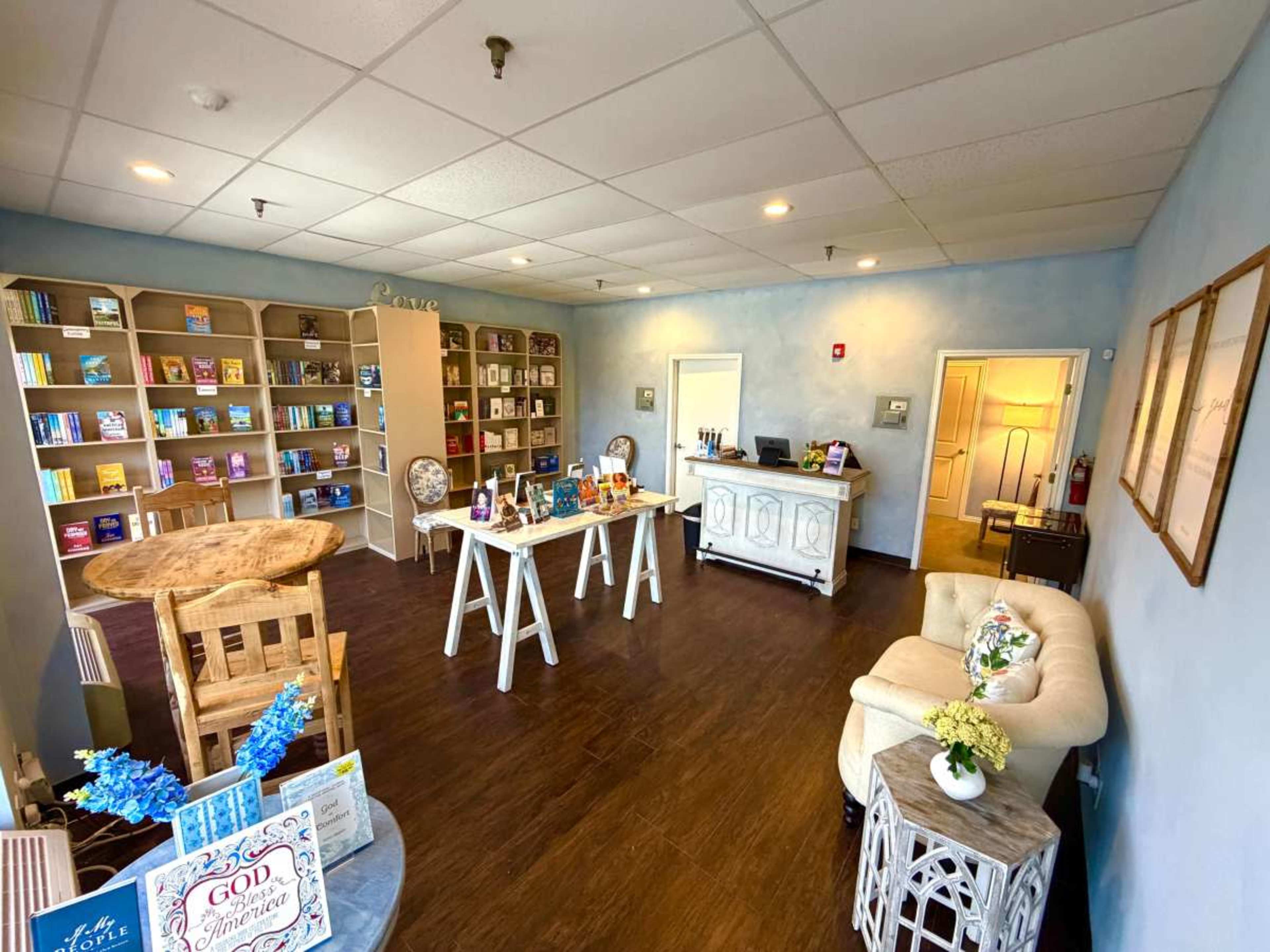 The image shows a cozy interior of a shop or a waiting area with wooden furniture, bookshelves filled with books, and a reception desk.