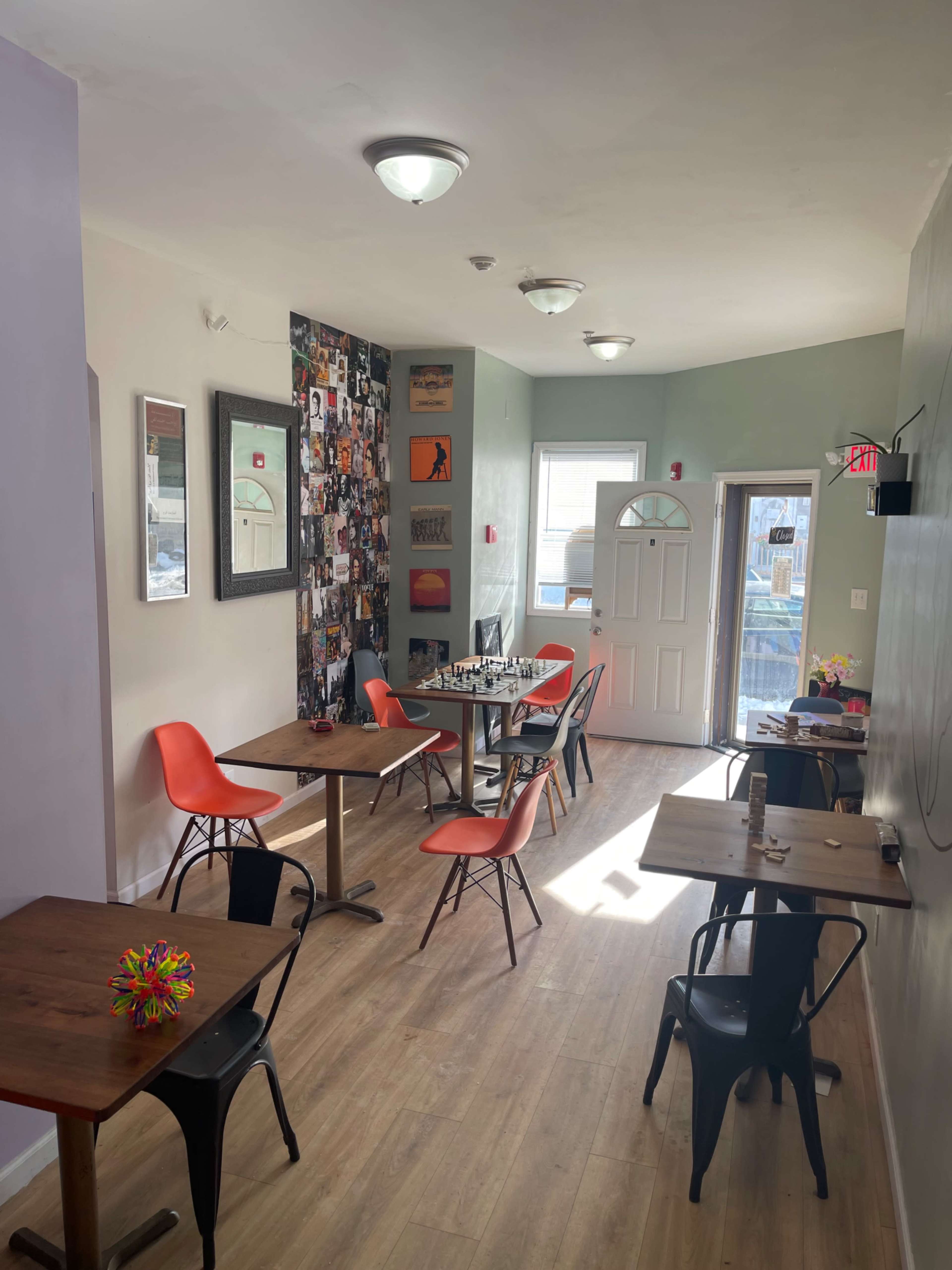 The image shows a modern cafe interior with several tables and chairs, featuring walls adorned with photographs and artwork.