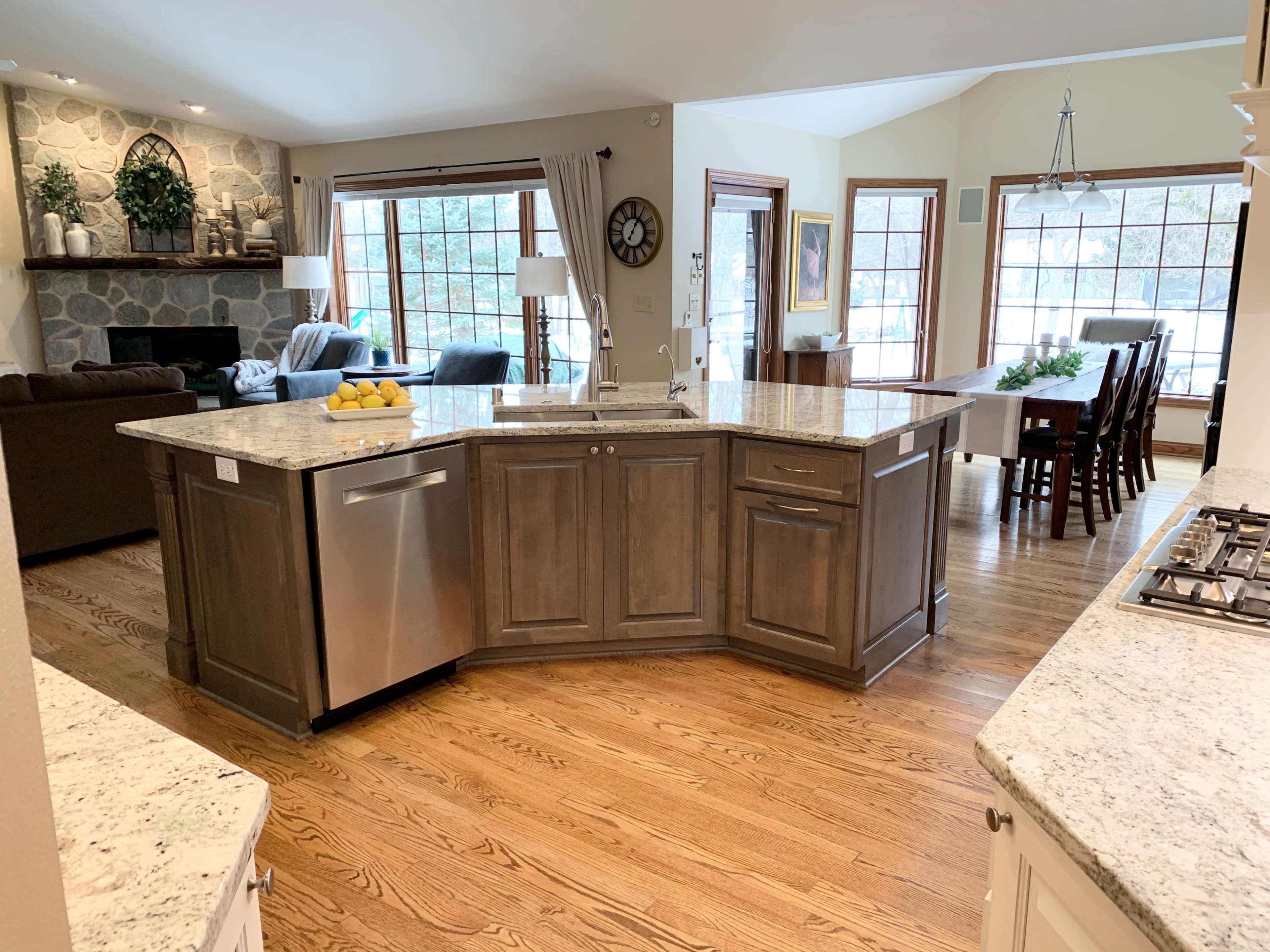 A spacious kitchen with a central island, featuring stone countertops and wooden cabinetry, adjacent to a comfortable living area with large windows.