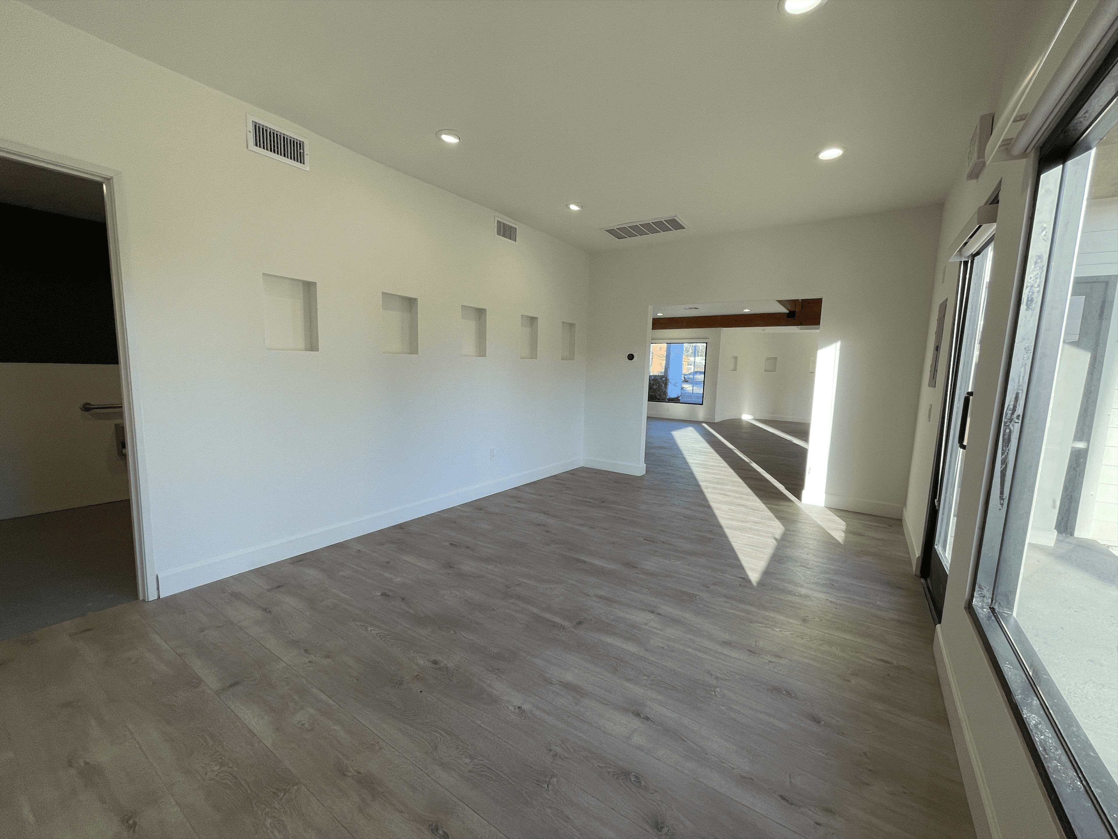 The image shows a bright, empty room with light-colored walls, a wooden floor, and several square recessed niches on one wall.