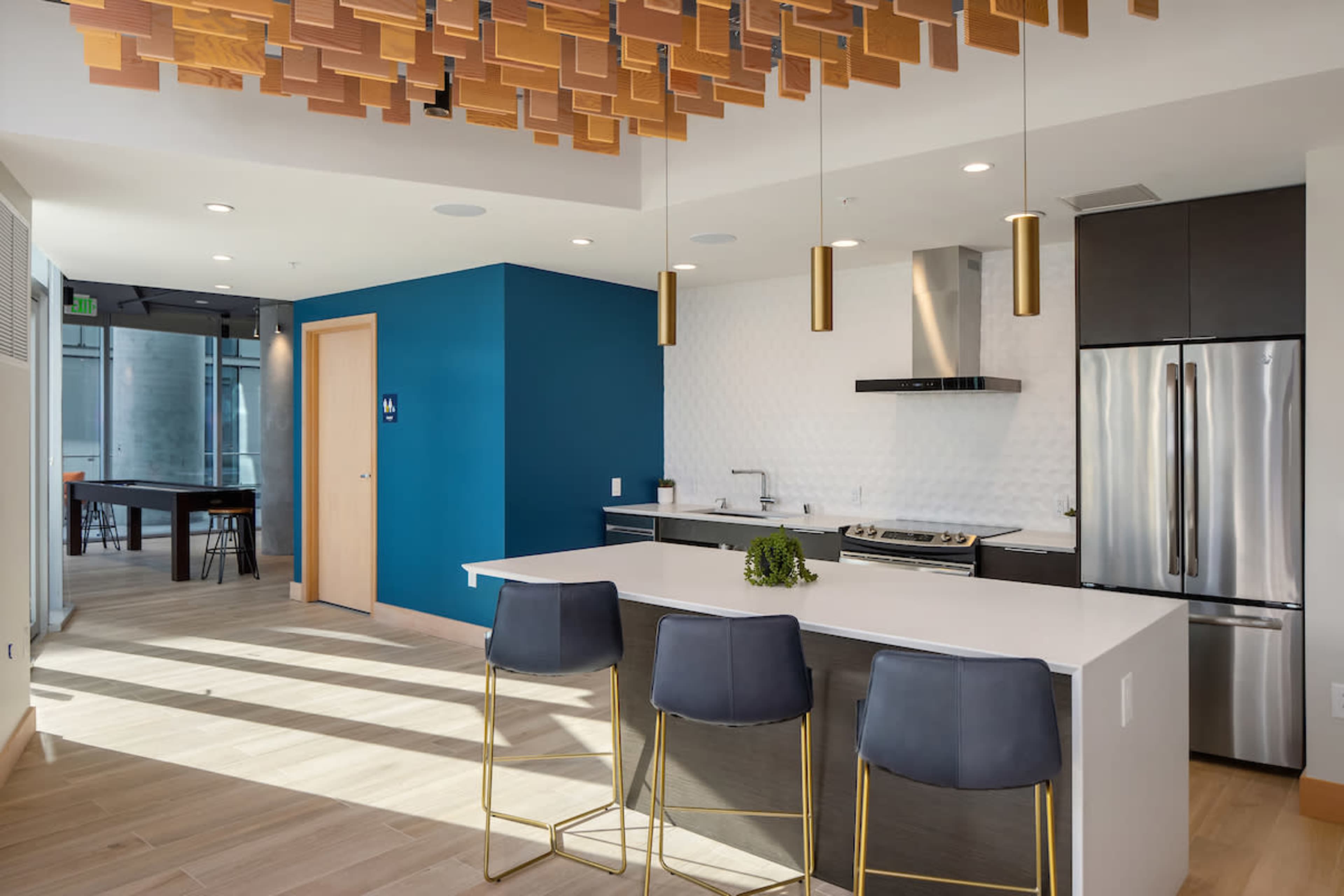 A modern kitchen features a central island with bar stools, sleek appliances, and an accent wall painted blue, illuminated by pendant lights.