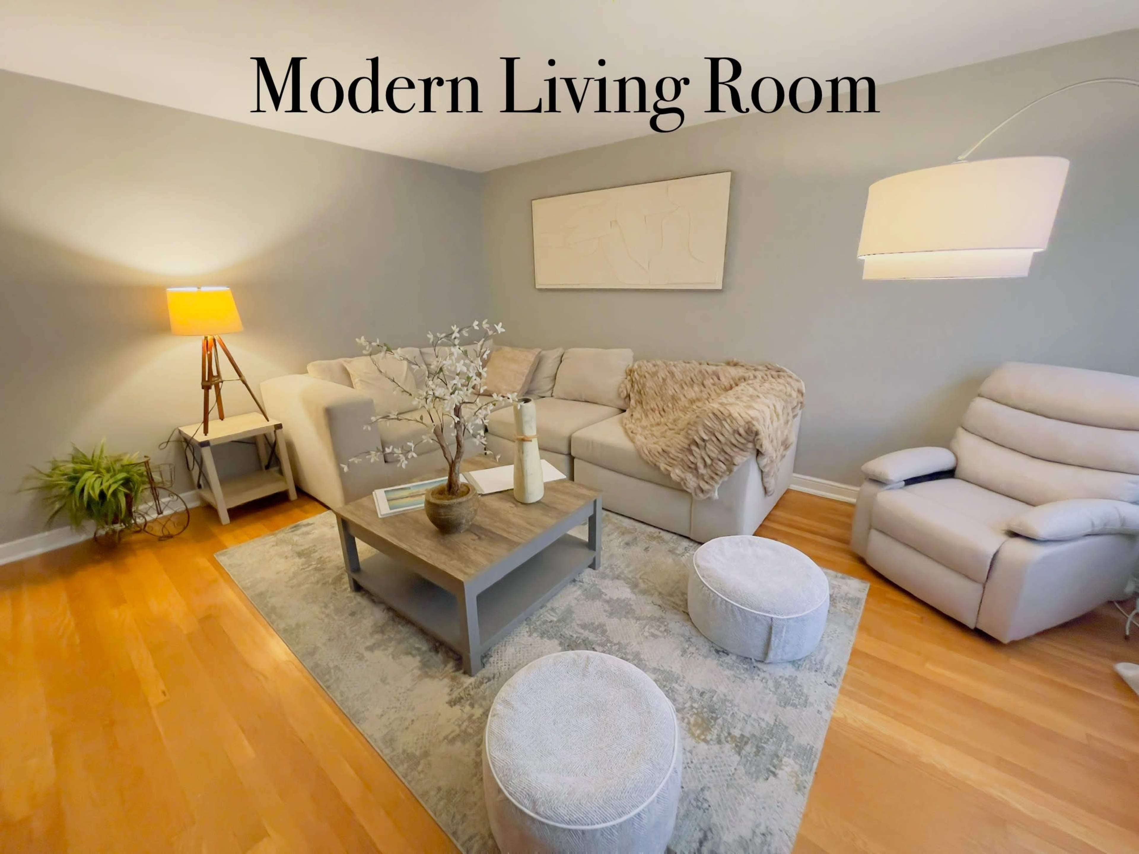 The image shows a modern living room featuring a sectional sofa, a coffee table, and a recliner, with a lamp and decorative elements on the table.