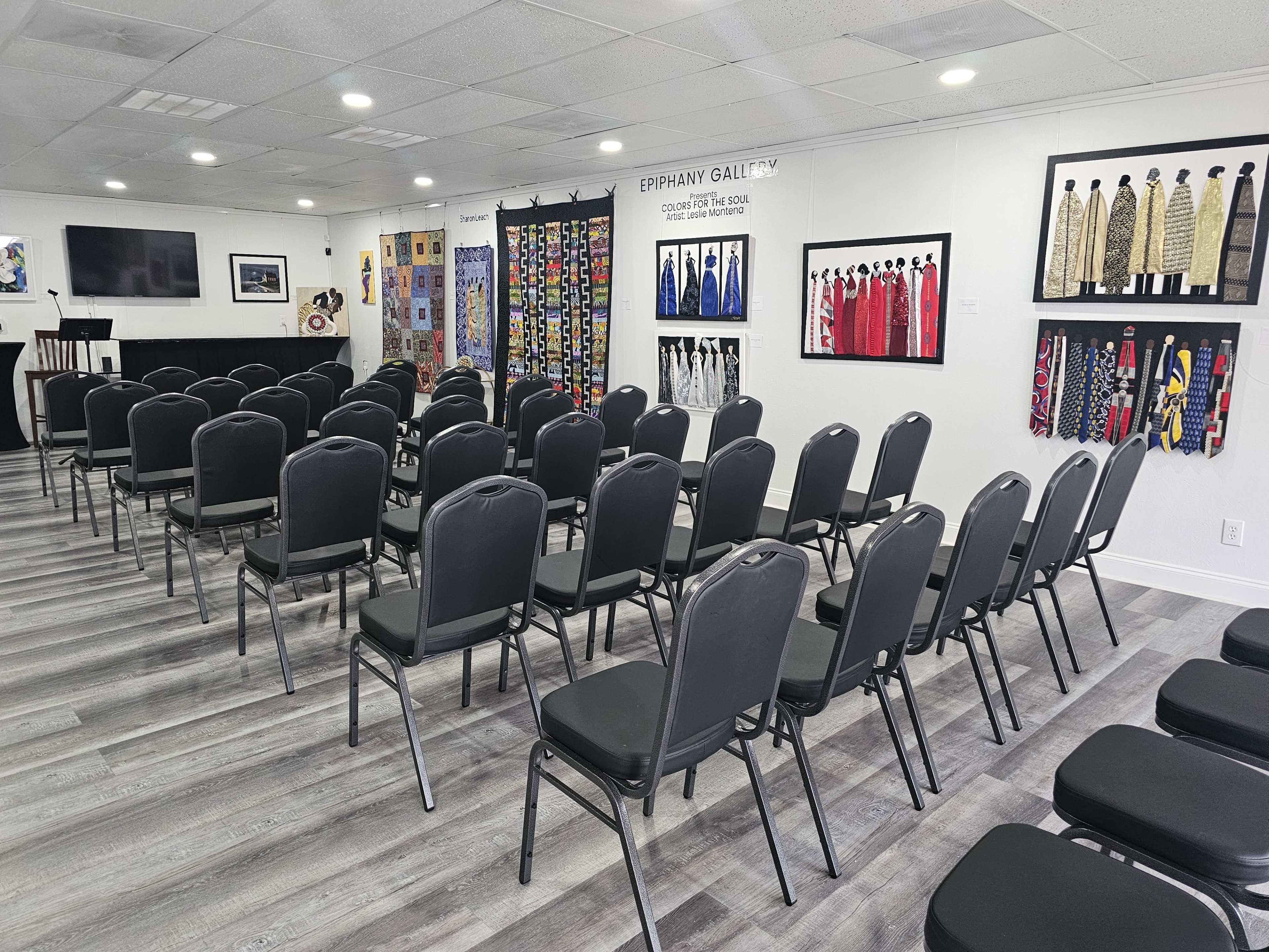 A seating arrangement of black chairs set up in a room with artworks displayed on the walls.