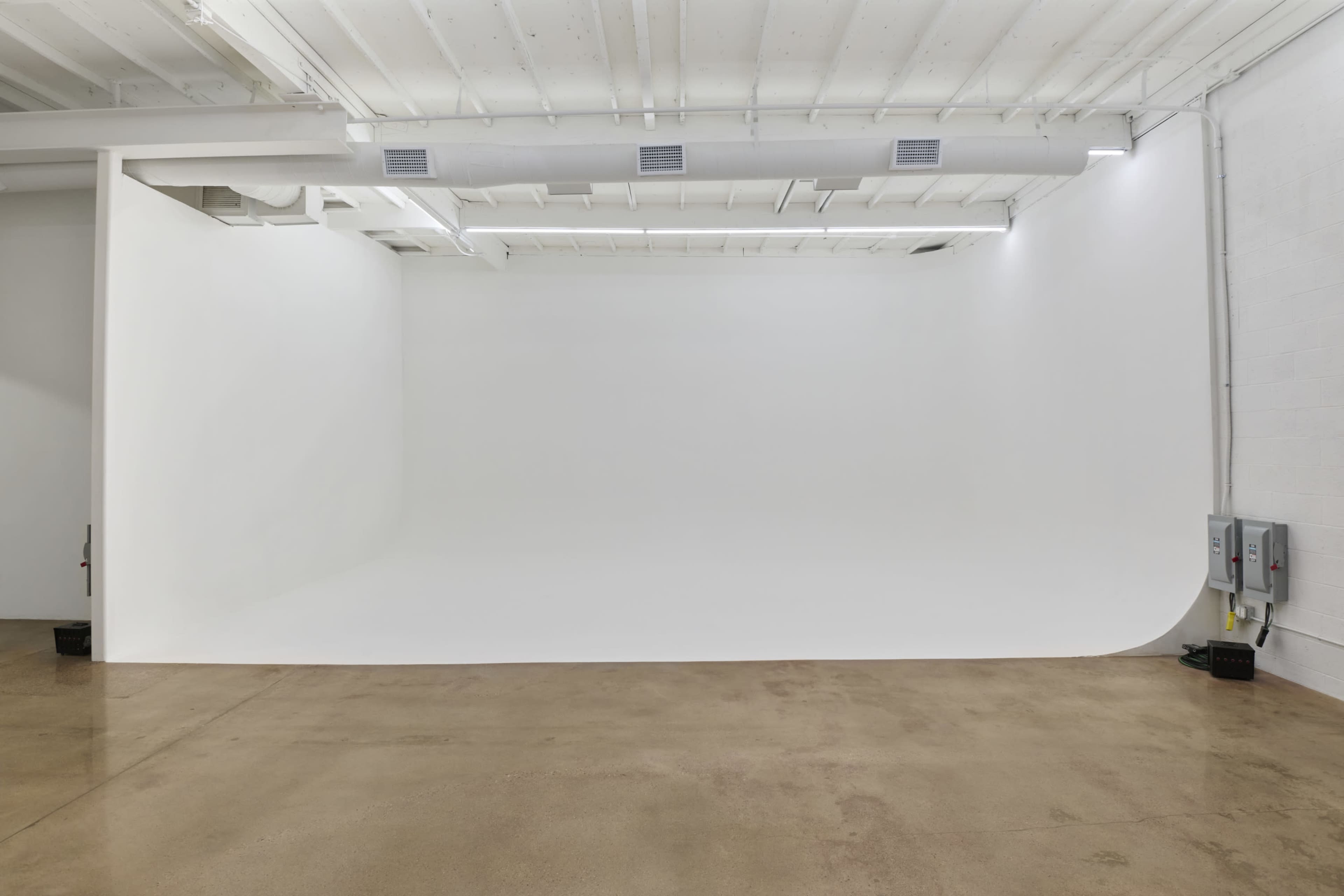 The image shows a spacious, minimalist studio with a seamless white backdrop and polished concrete flooring.
