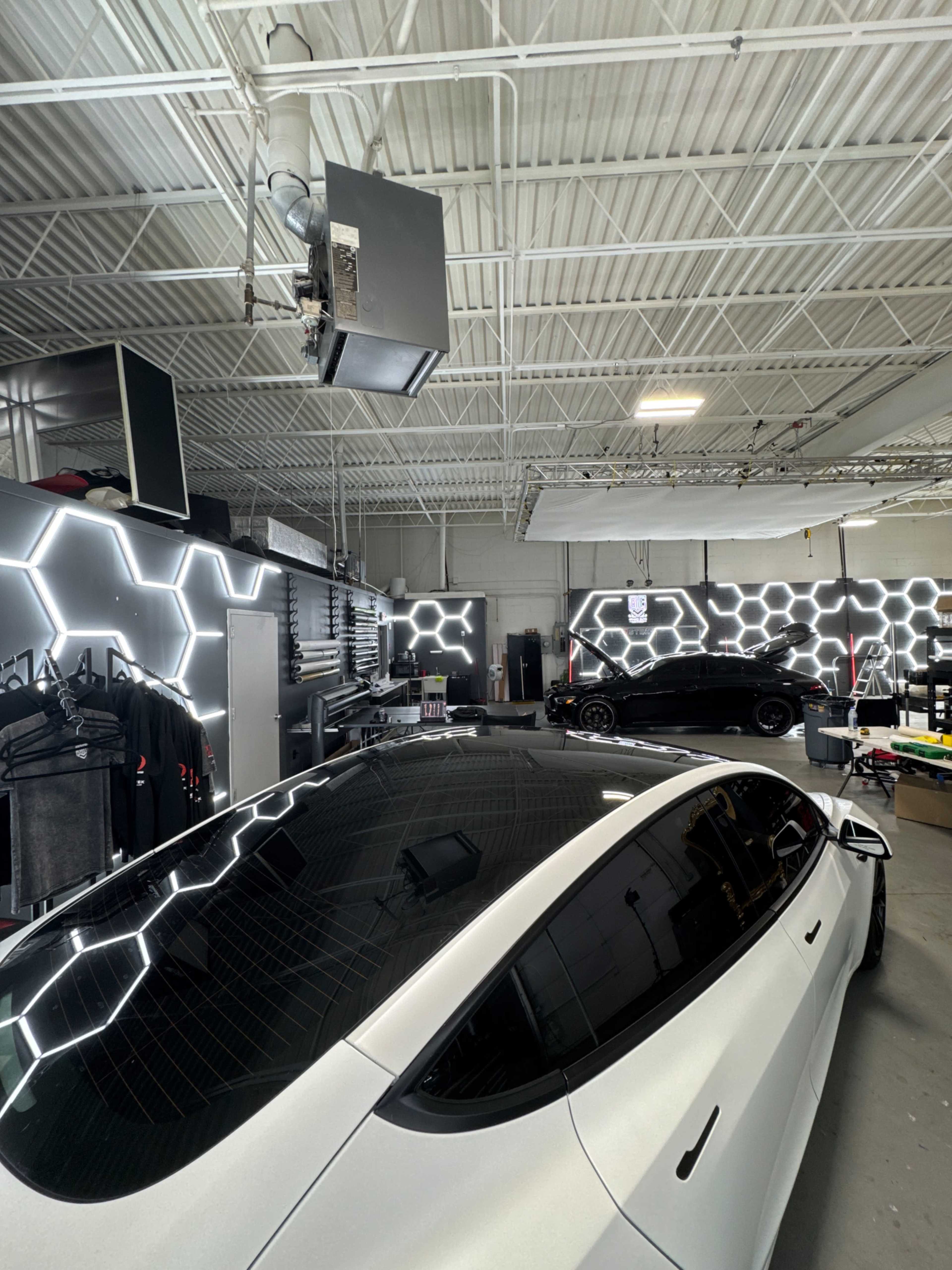 The image shows a modern automotive detailing shop featuring sleek cars, a specialized work area with tools, and geometric LED lighting on the walls.