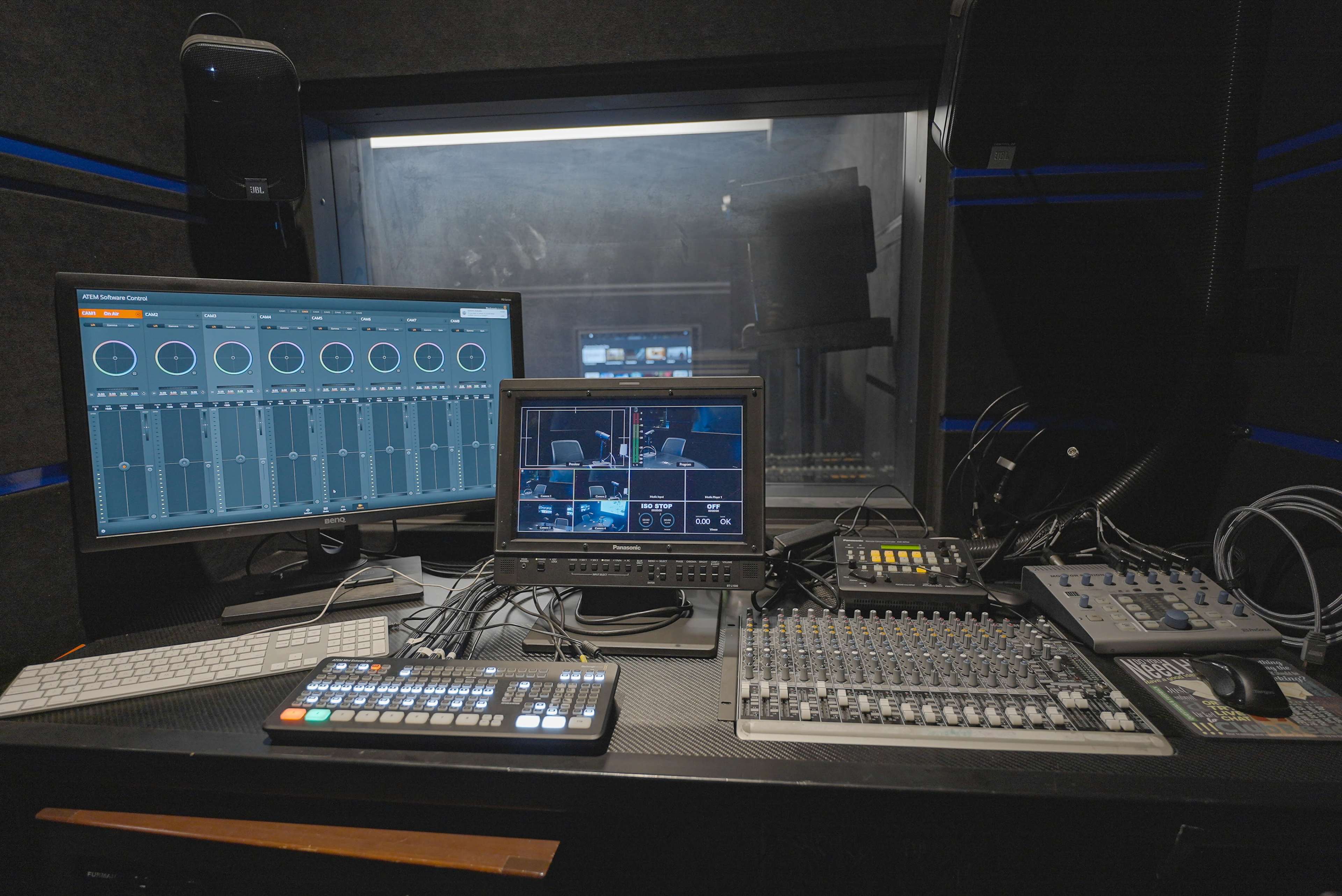 This image shows a video production control room with multiple monitors, a mixing console, and various cables.