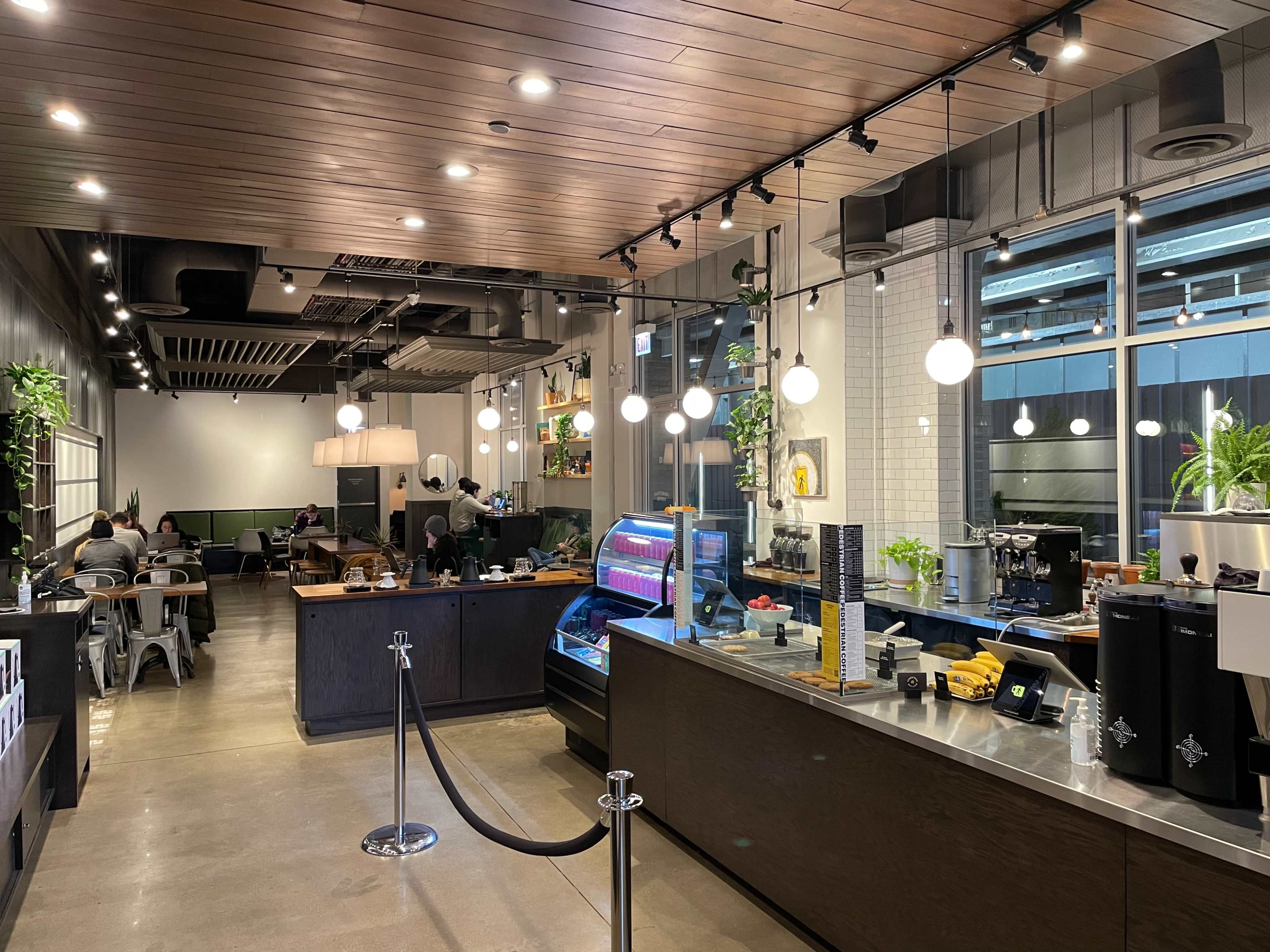 The image shows a modern café interior with a sleek counter, hanging lights, and patrons seated in various areas.