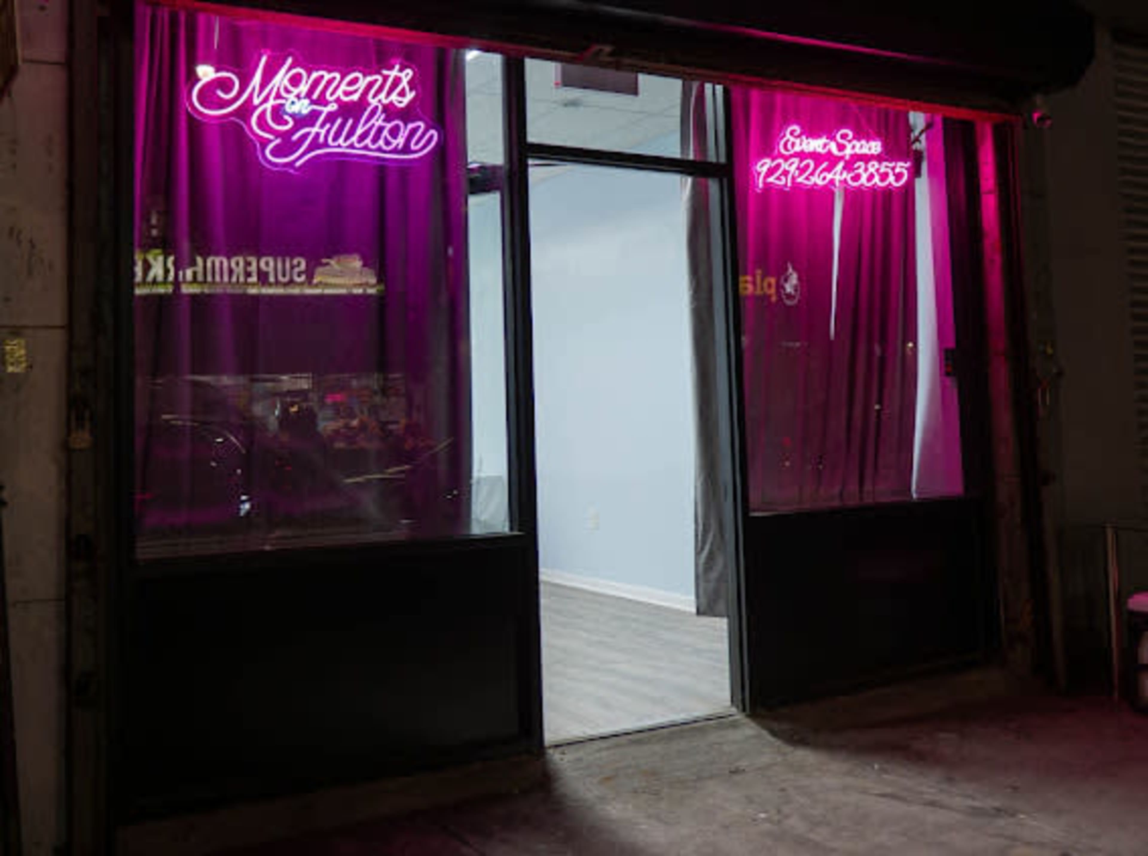The image shows a storefront with a glass door, featuring pink neon signs that read "Moments & Fulton" and a phone number for rental inquiries.