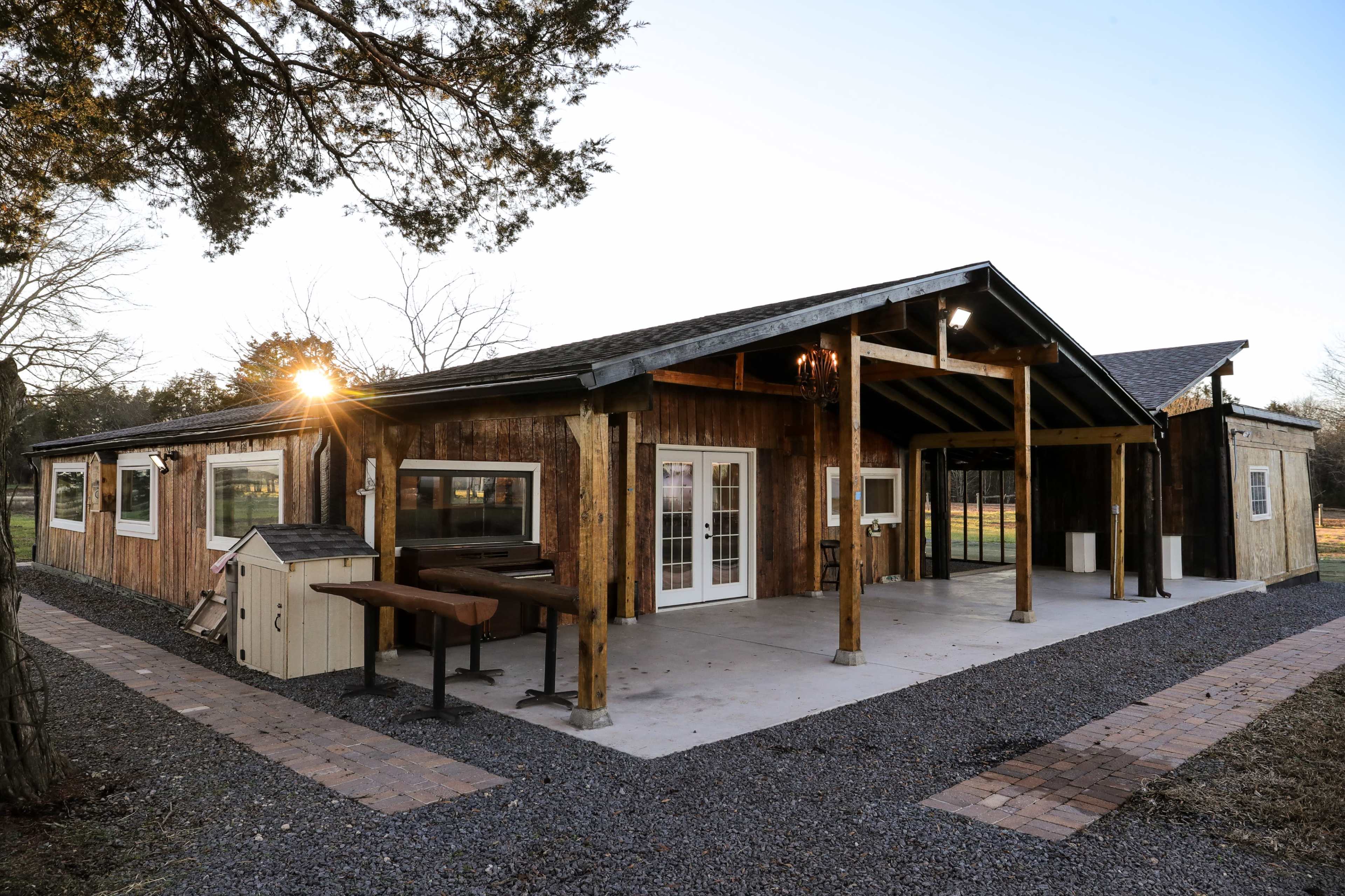 A rustic, single-story building with wooden siding, large windows, and a spacious outdoor area featuring a stone pathway and landscaping.