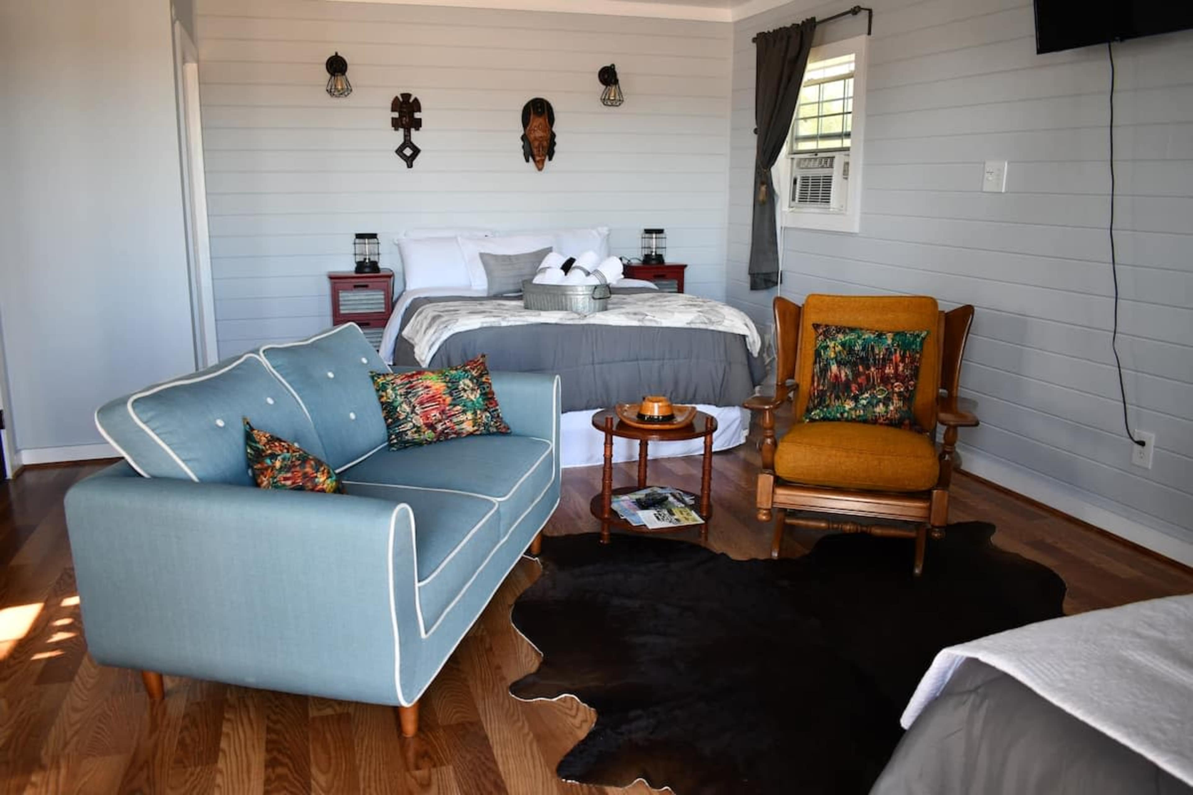 A room featuring a bed, a blue sofa, a wooden chair, and a coffee table on a rug.