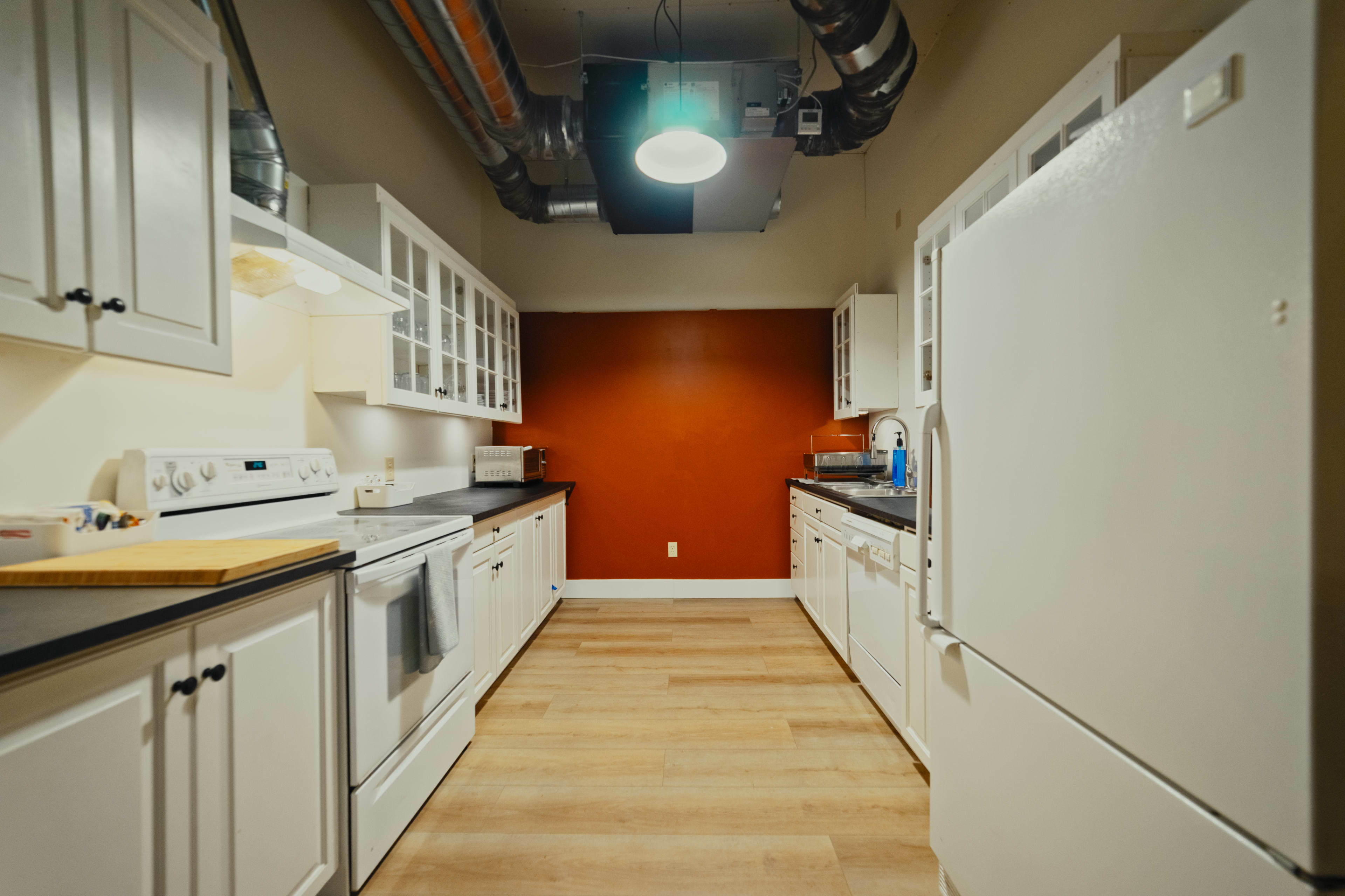 A kitchen features white cabinets, stainless steel appliances, and a red accent wall, with a light fixture hanging from the ceiling.