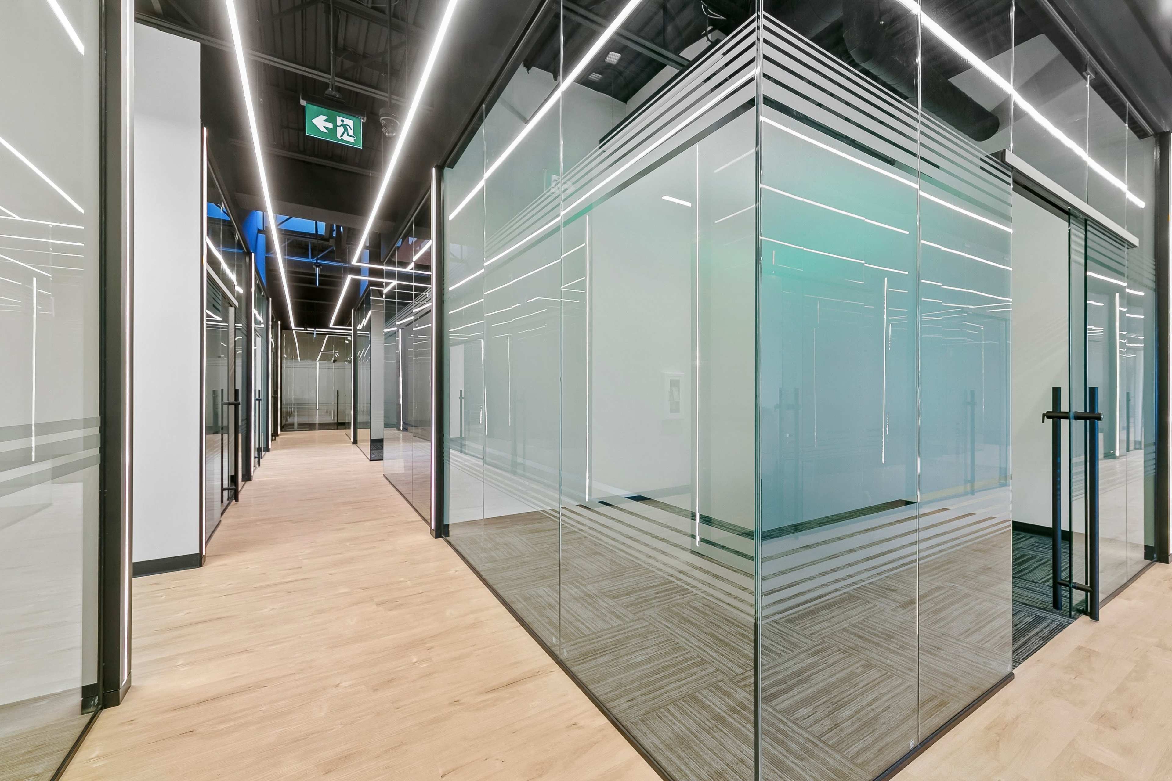 The image shows a modern office interior with glass-walled conference rooms and a hallway featuring wooden flooring.