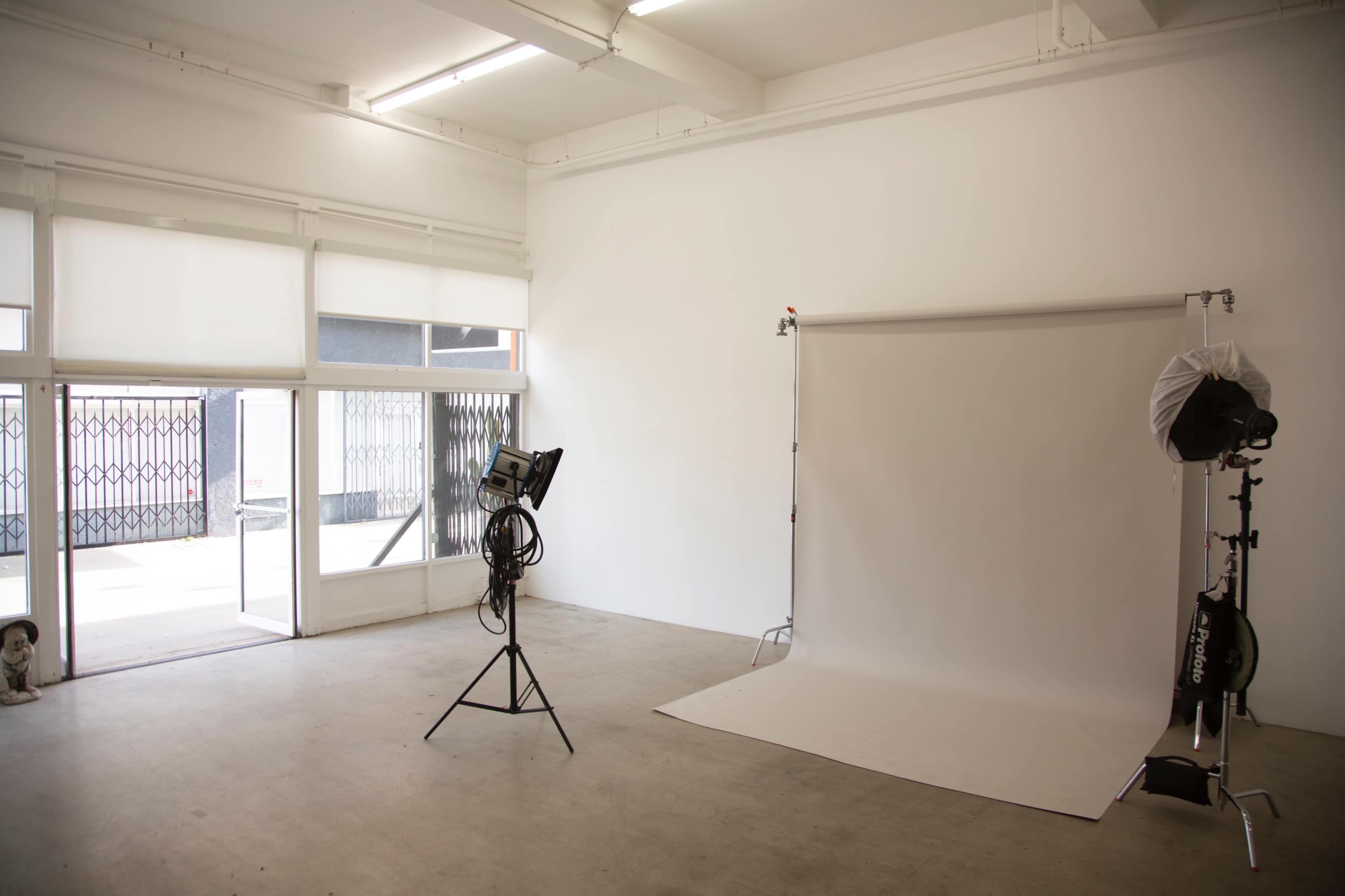 A photography studio with a white backdrop, lighting equipment, and large windows allowing natural light to enter.