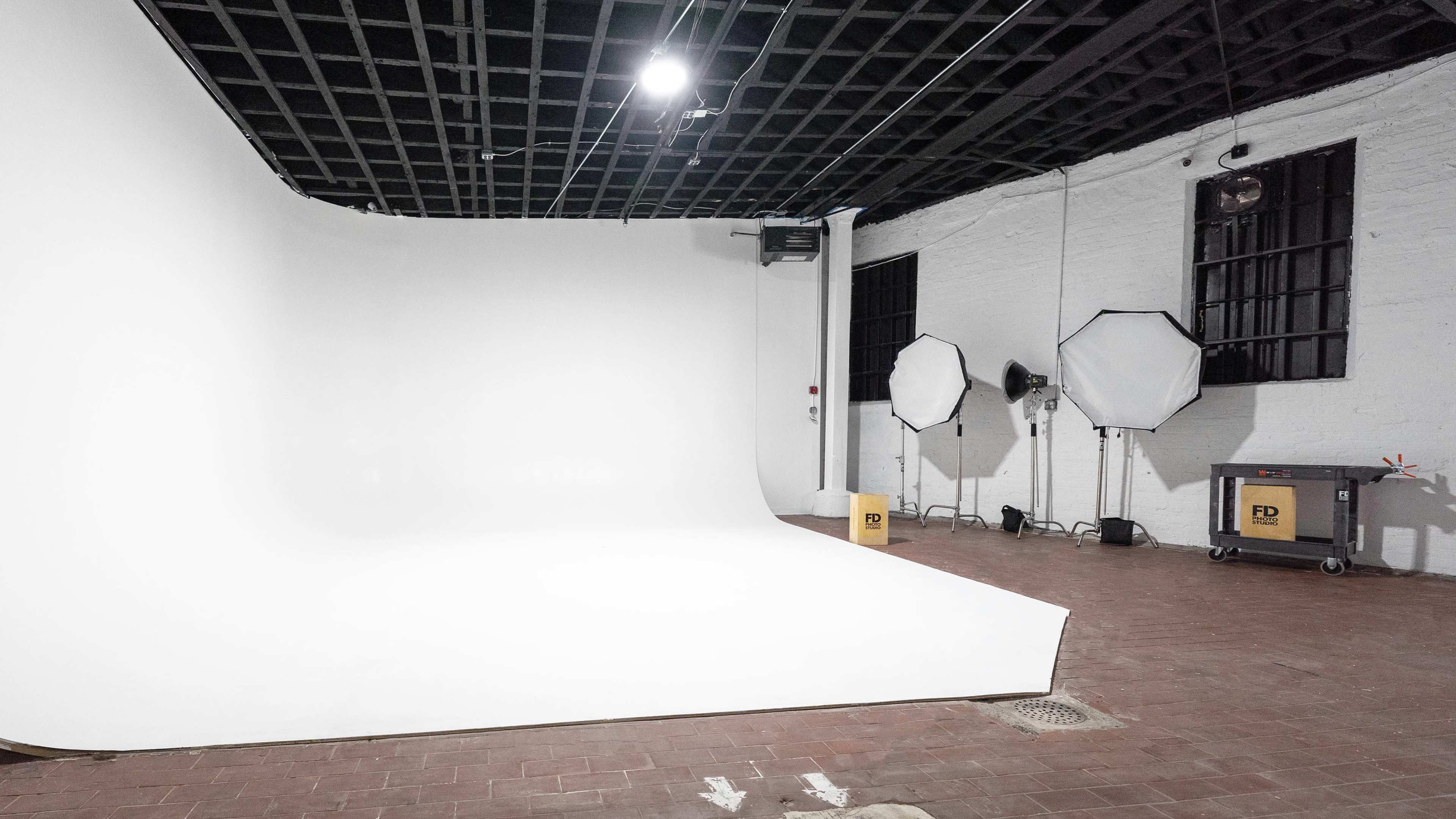 A photography studio with a seamless white backdrop, softbox lights, and a cart in a well-lit, empty space.