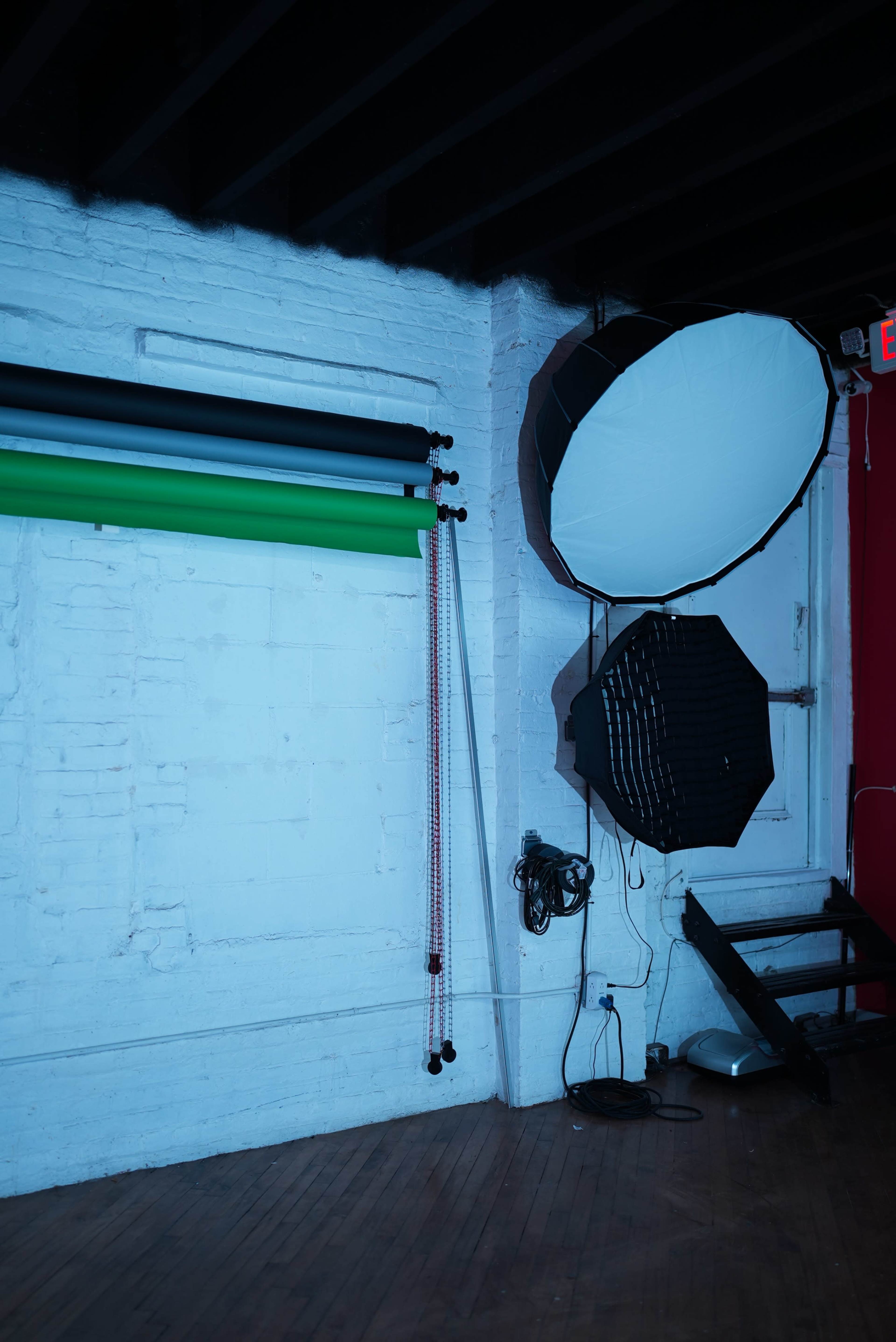 The image features a photography studio with colorful backdrop rolls, lighting equipment, and a wooden floor.