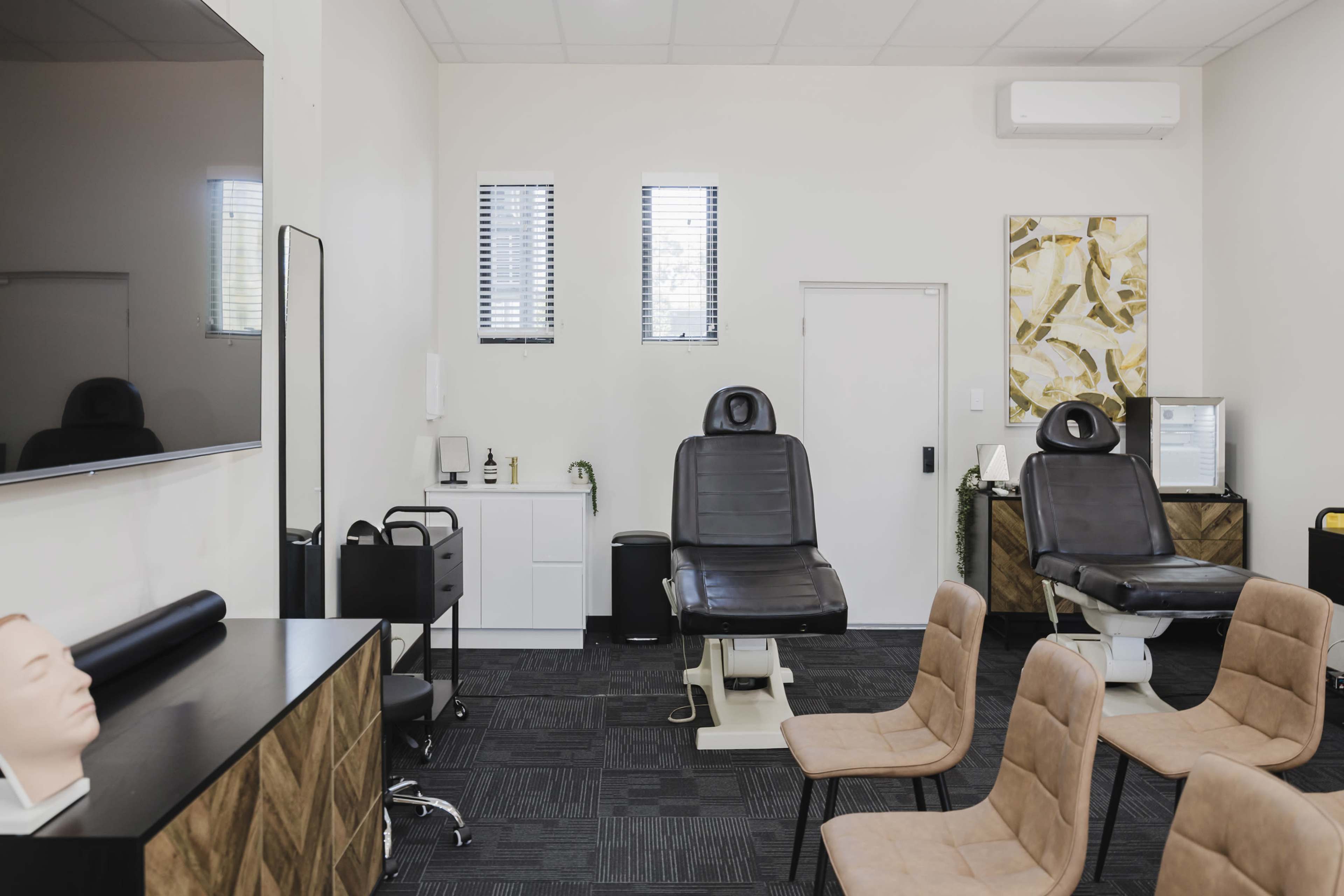 The image shows a minimally furnished treatment room with two reclining chairs, a mirror, and several chairs arranged in a waiting area.