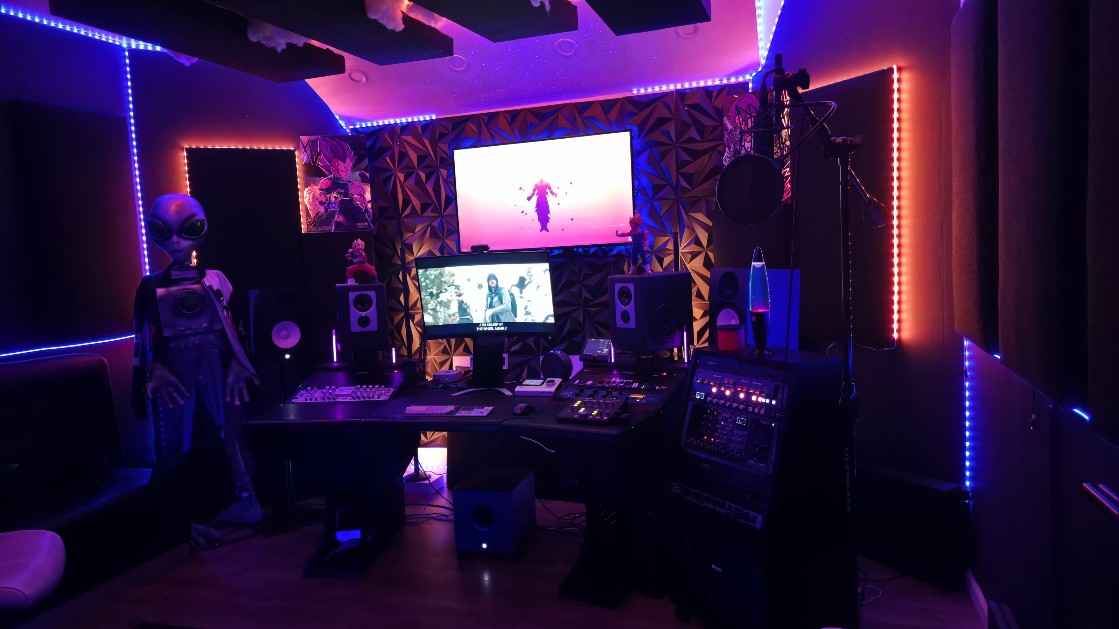 The image depicts a music studio with illuminated walls, a large screen displaying visuals, and various audio equipment arranged around a central workspace.
