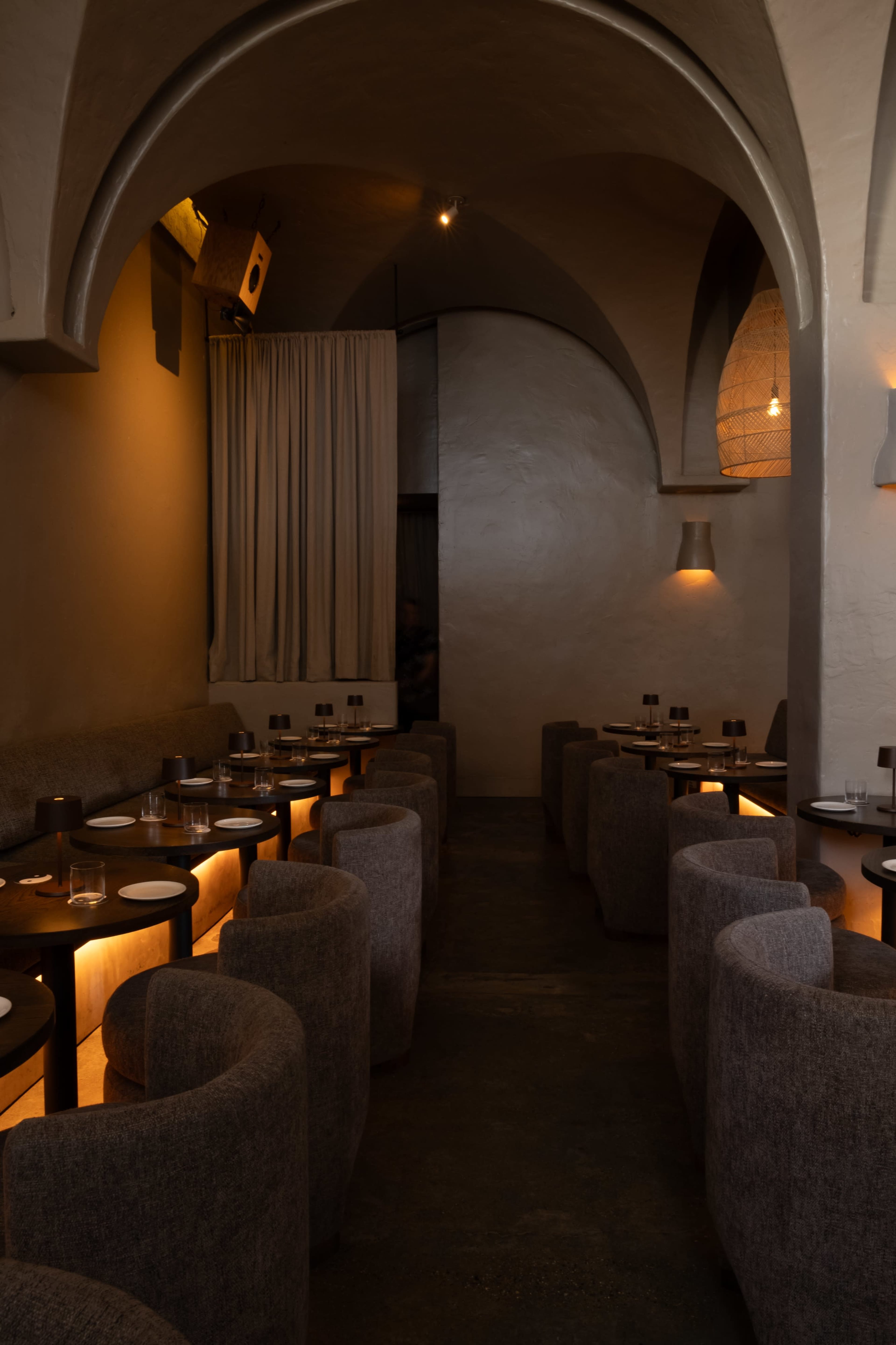 The interior of a restaurant features rows of circular booths along the walls, with subdued lighting and arched ceilings.