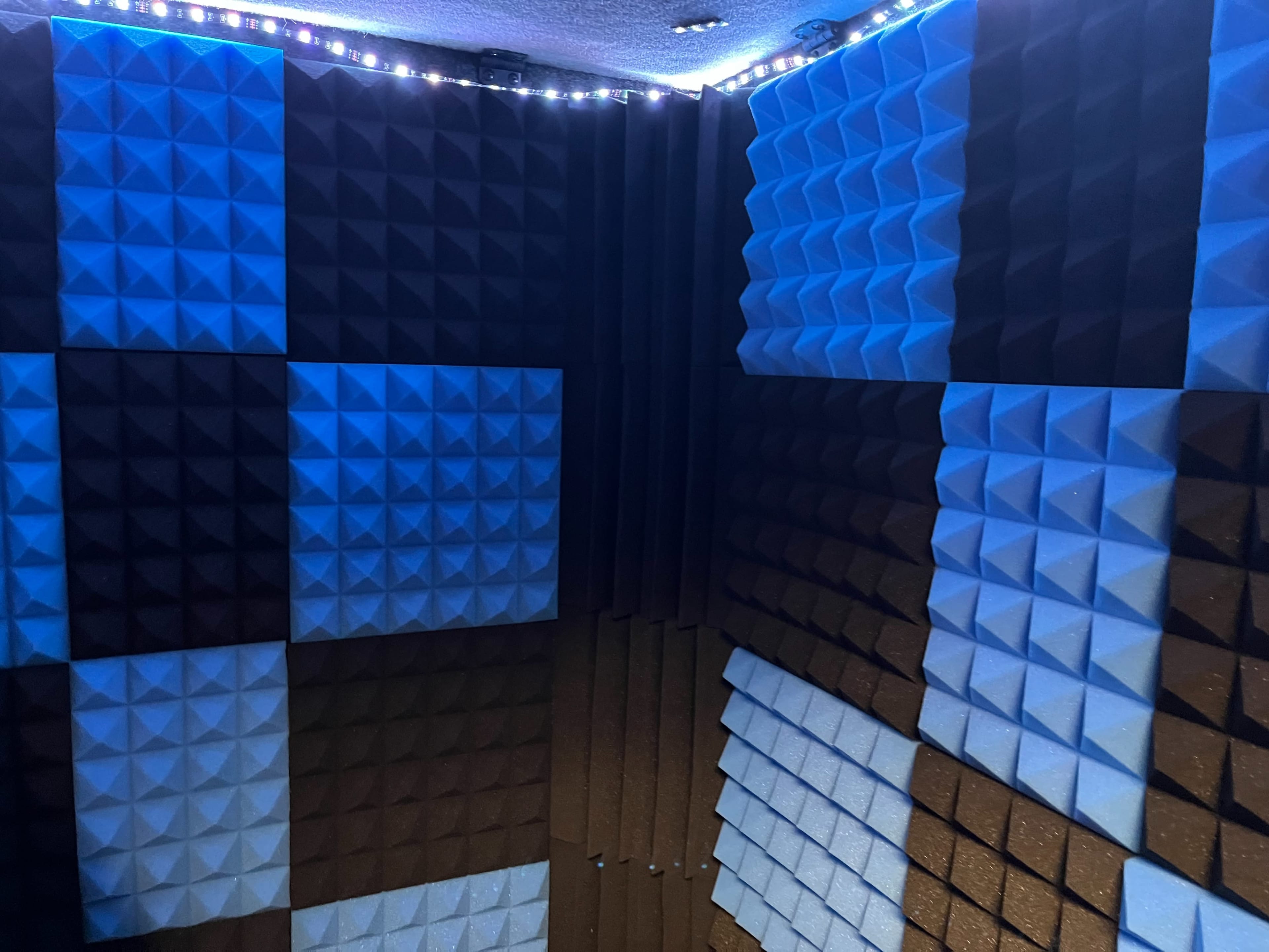 A corner of a soundproof room with blue and dark acoustic foam panels arranged in a geometric pattern.