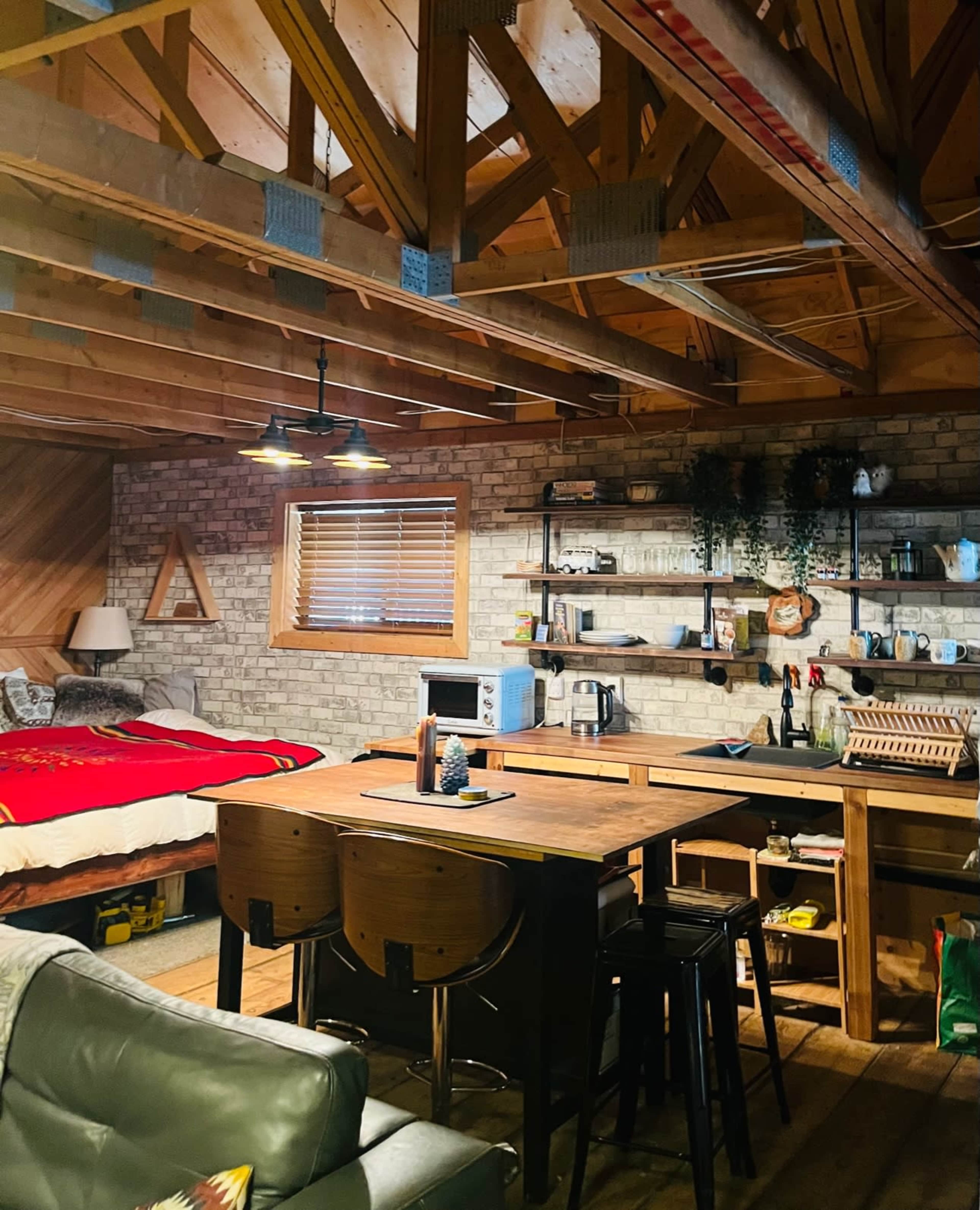 A cozy cabin interior features a bedroom area with a bed, a living space with a sofa, and a kitchen area complete with a table and various appliances.