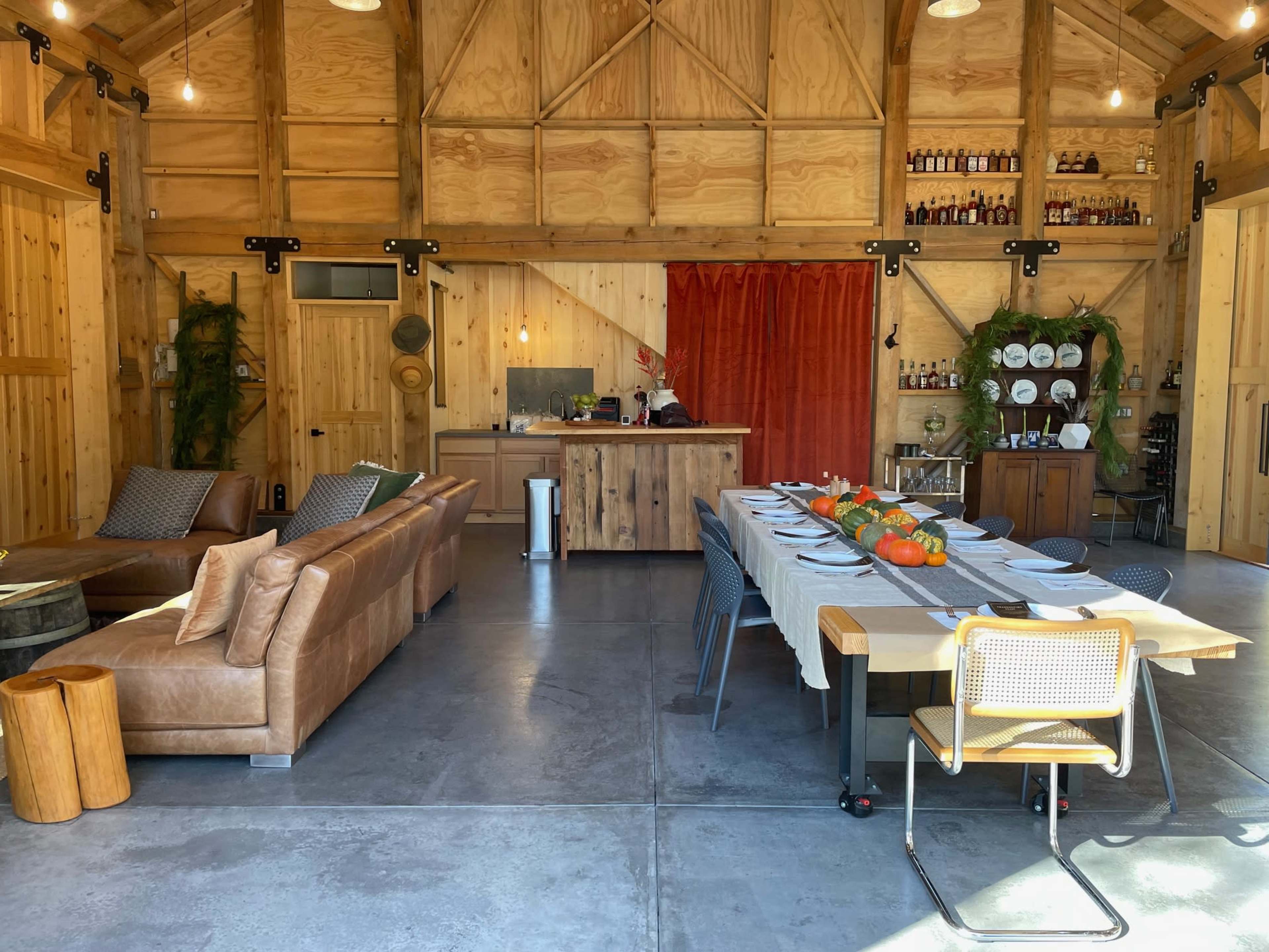 The interior of a wooden-finished gathering space features a large dining table set with dishes and seasonal decorations, alongside a lounge area with a leather sofa.