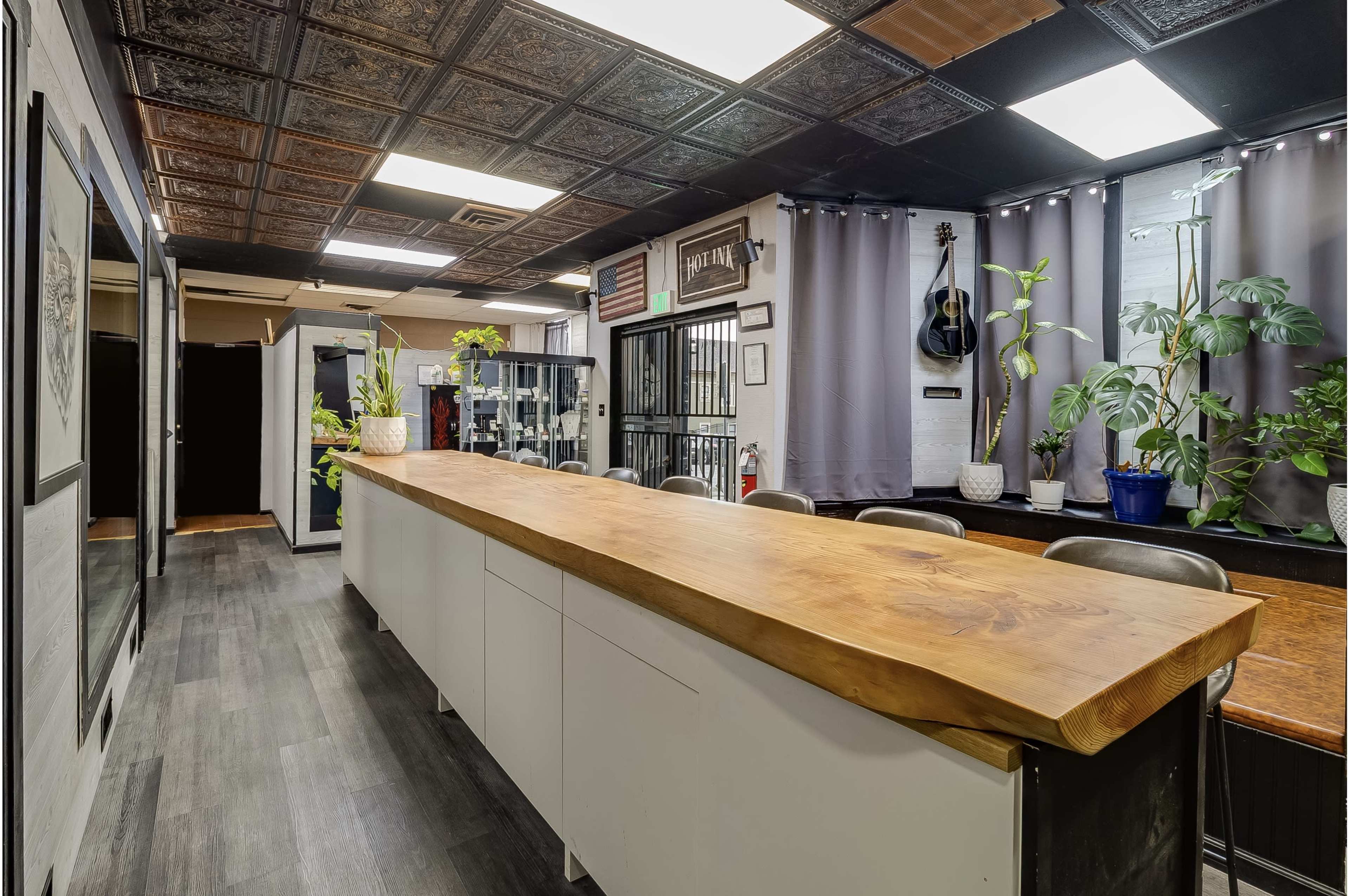 The image shows a modern reception area with a long wooden counter, potted plants, and a guitar hanging on the wall.