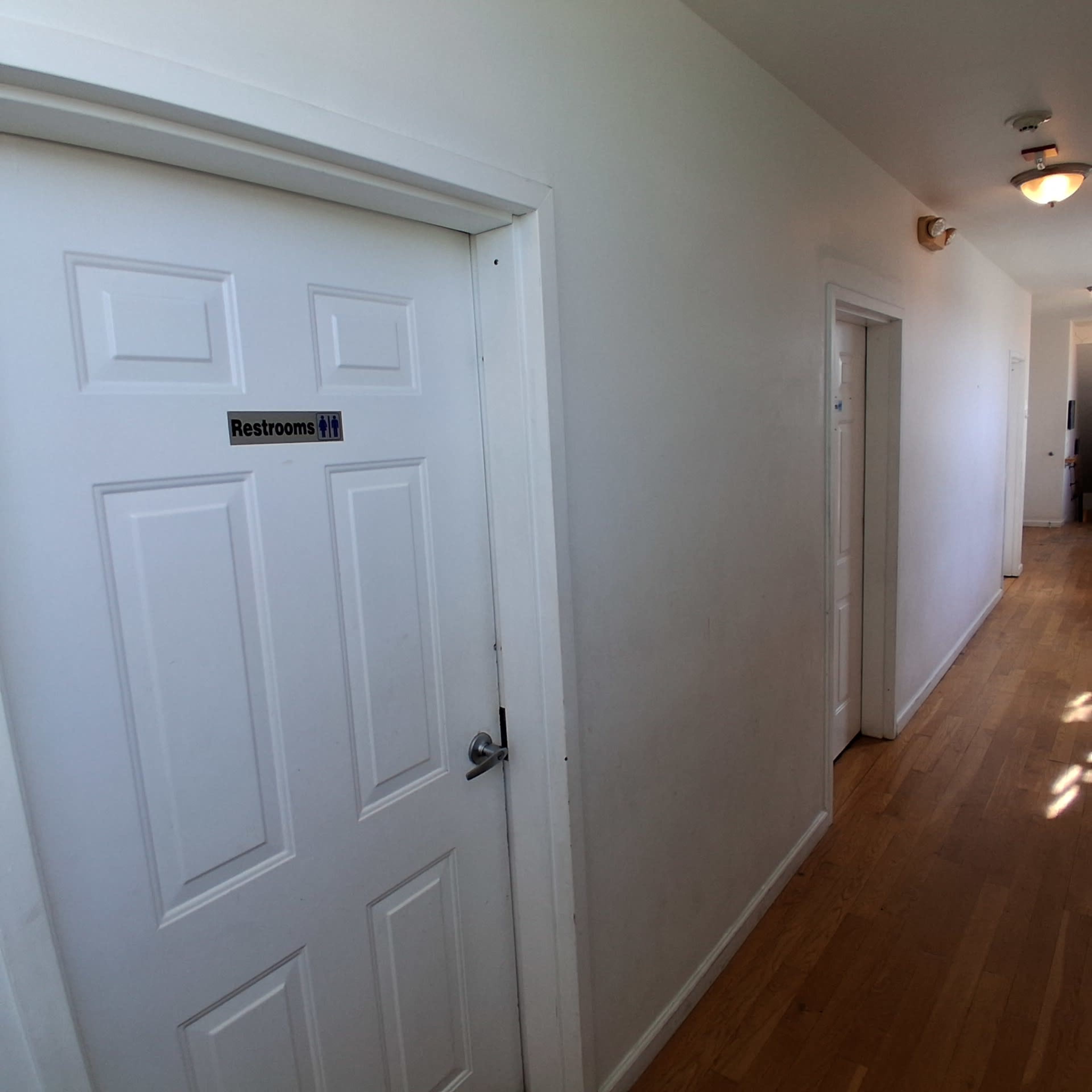 The image shows a narrow hallway with two closed doors on one side, one of which is labeled "Restrooms."