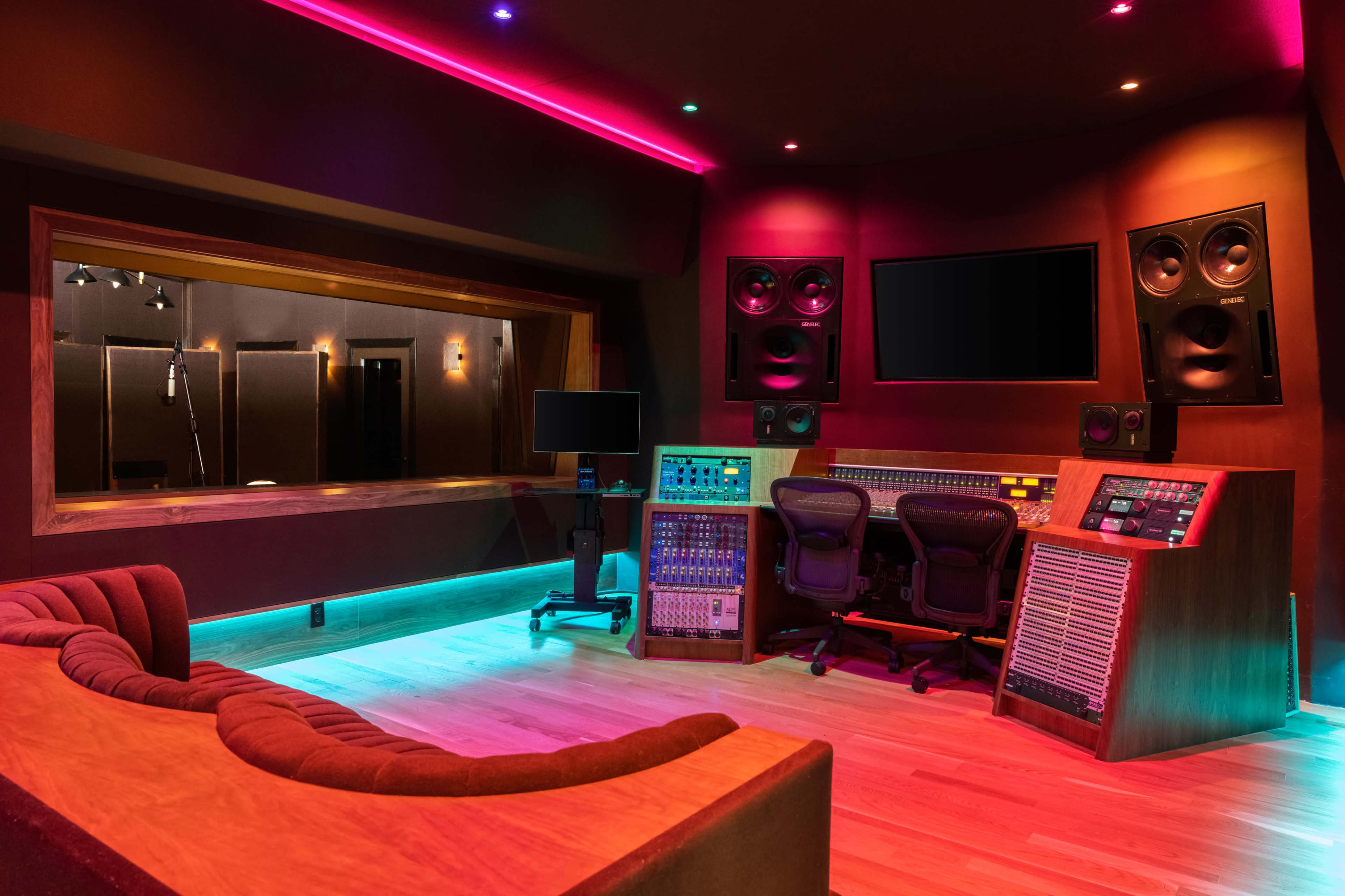 The image shows a modern music recording studio with sound equipment, a control desk, and acoustic panels, illuminated by colorful LED lights.