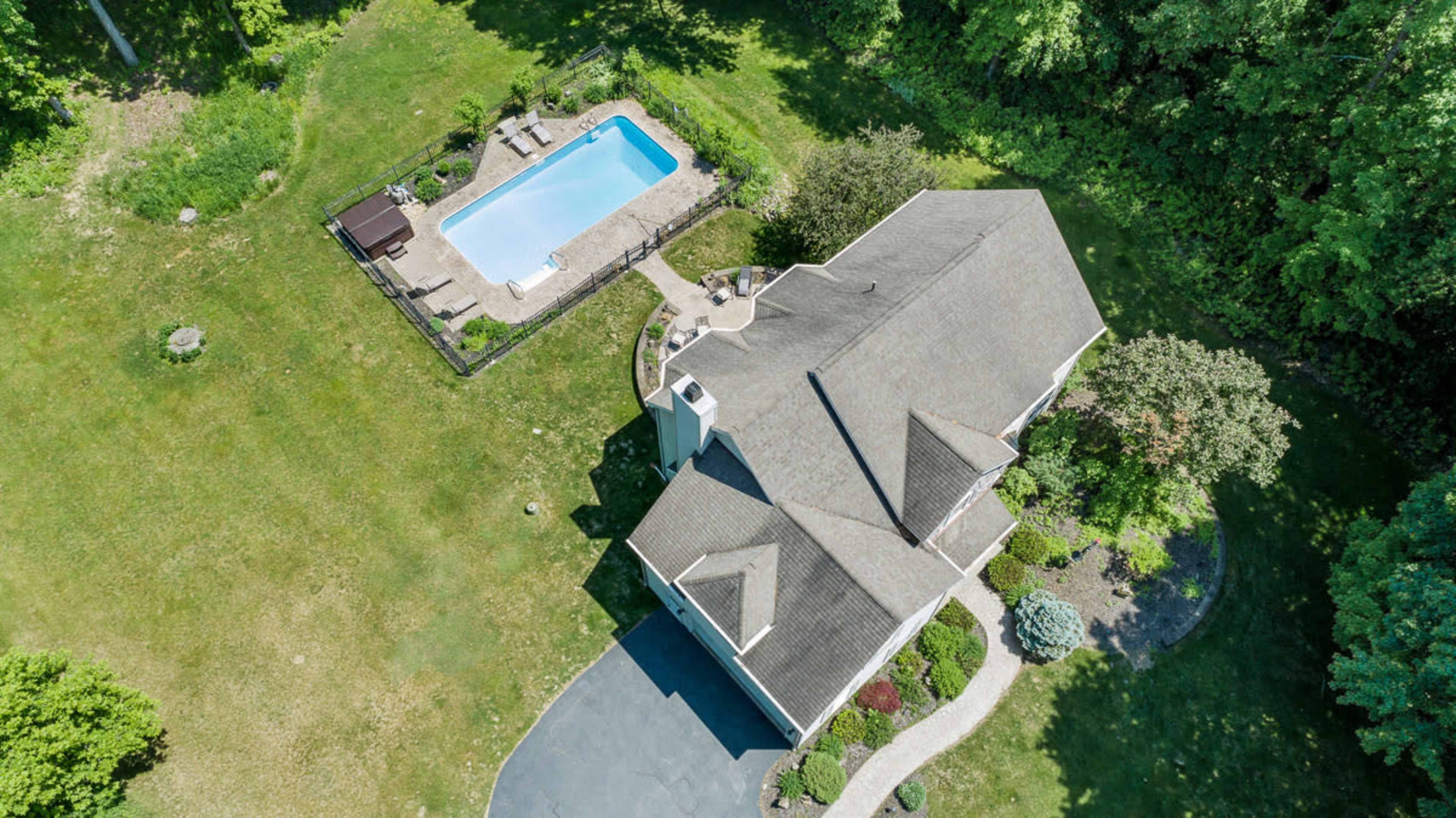 An aerial view shows a house with a gray roof, a patio, and a rectangular swimming pool surrounded by a grassy yard.
