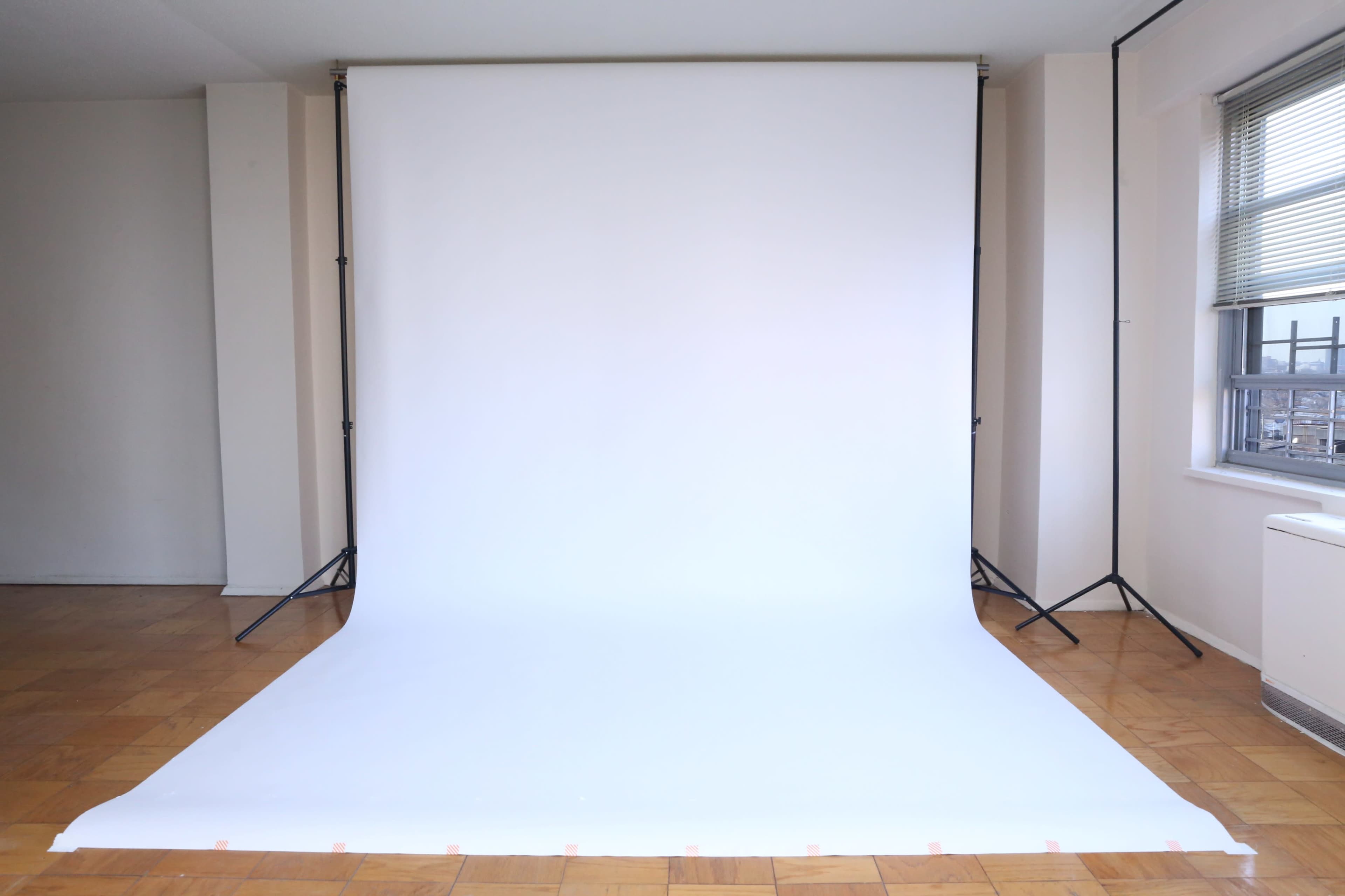 A large white backdrop set up in a room with wooden flooring and a window.