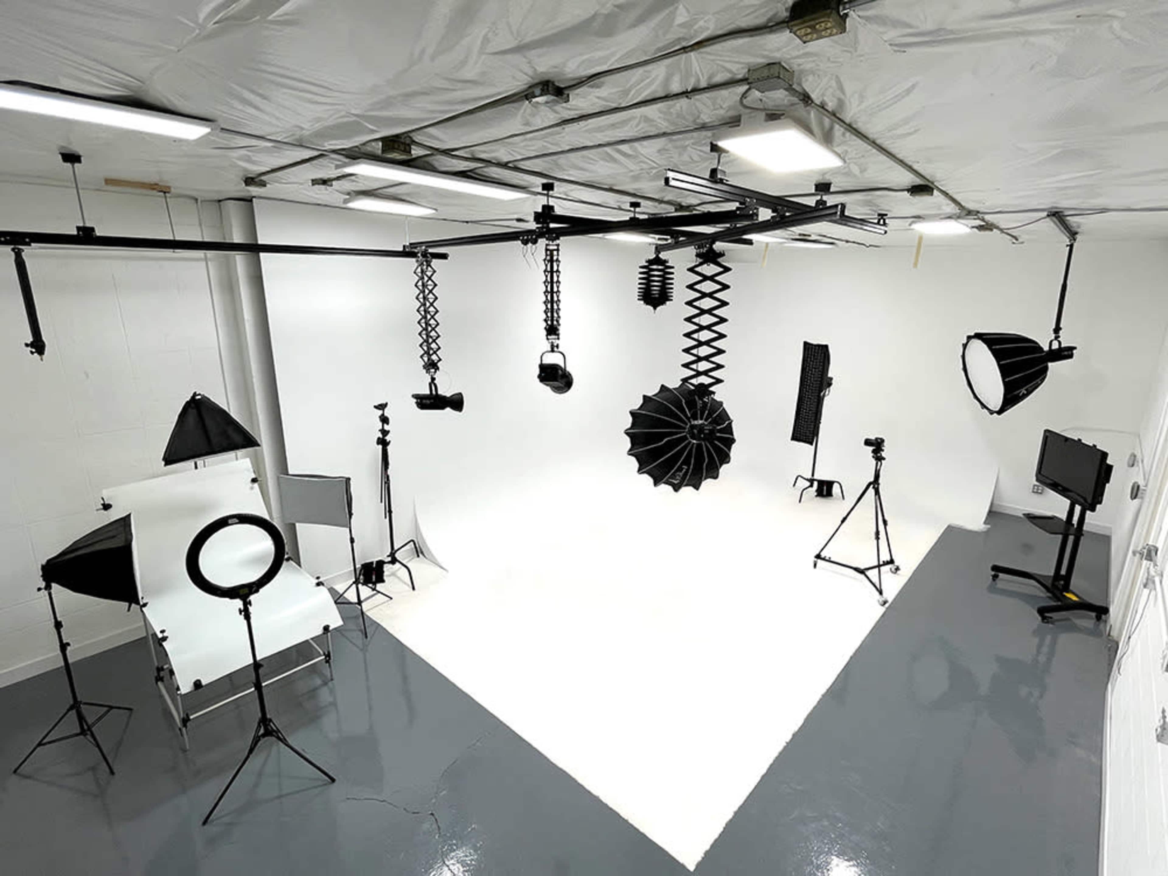 A photography studio with various lighting equipment, backdrops, and stands arranged in a white-walled space.