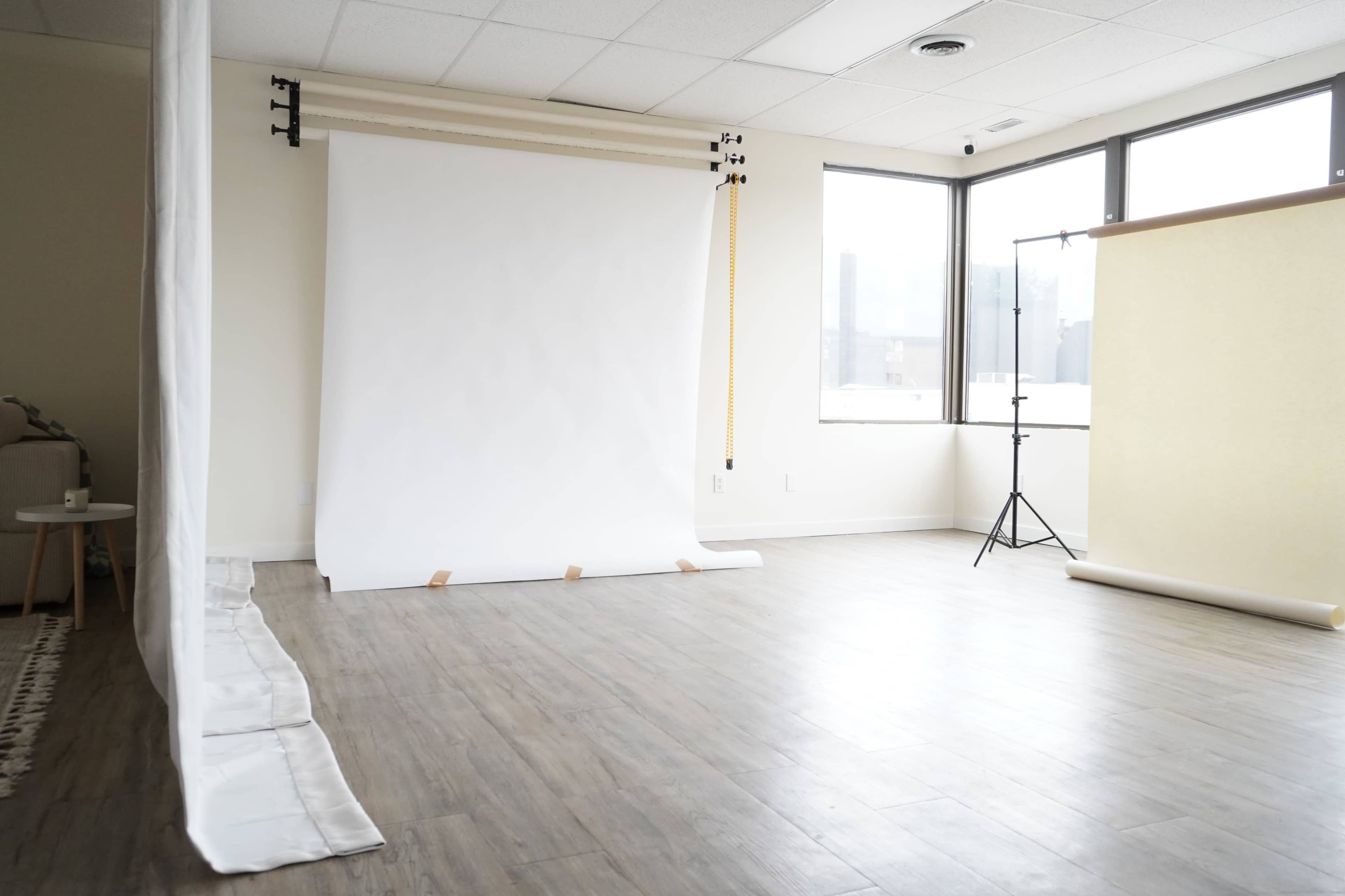 A spacious studio with a white backdrop, wooden flooring, and minimal furnishings.