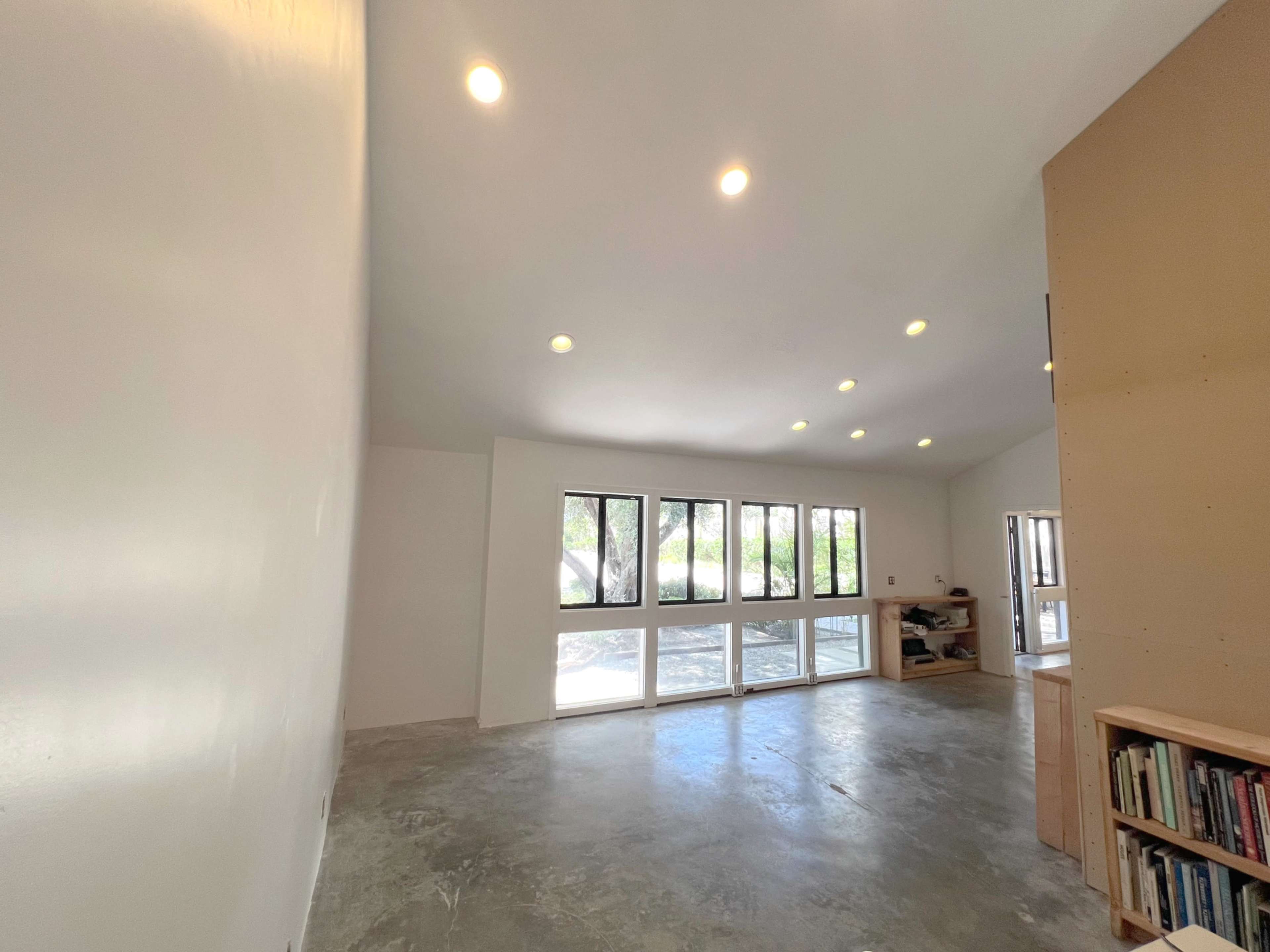 The image shows a spacious, well-lit room with a concrete floor and large windows that open to an outdoor view.