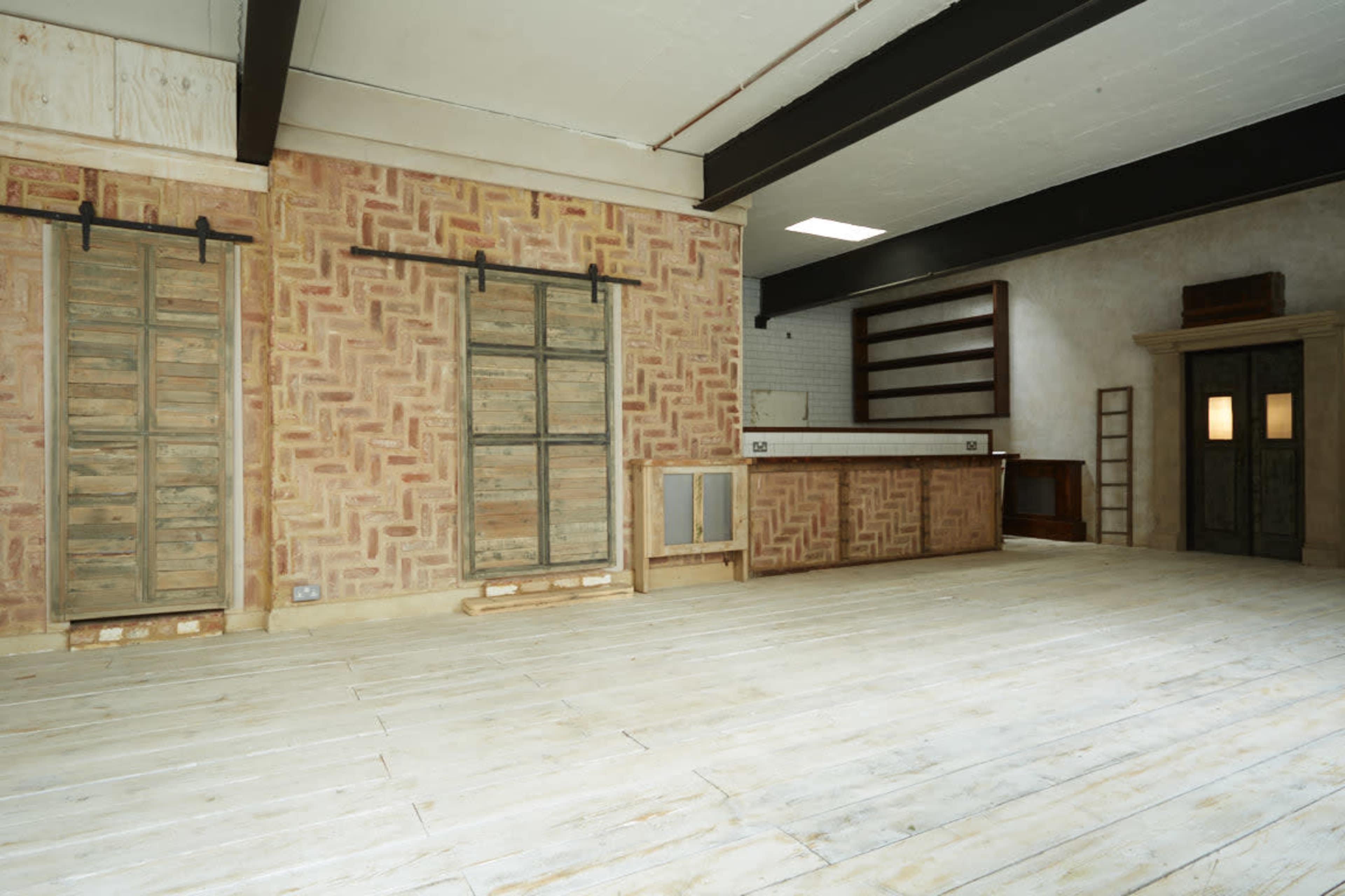 An empty interior space with a patterned brick wall, sliding wooden doors, and a wooden counter along one side.