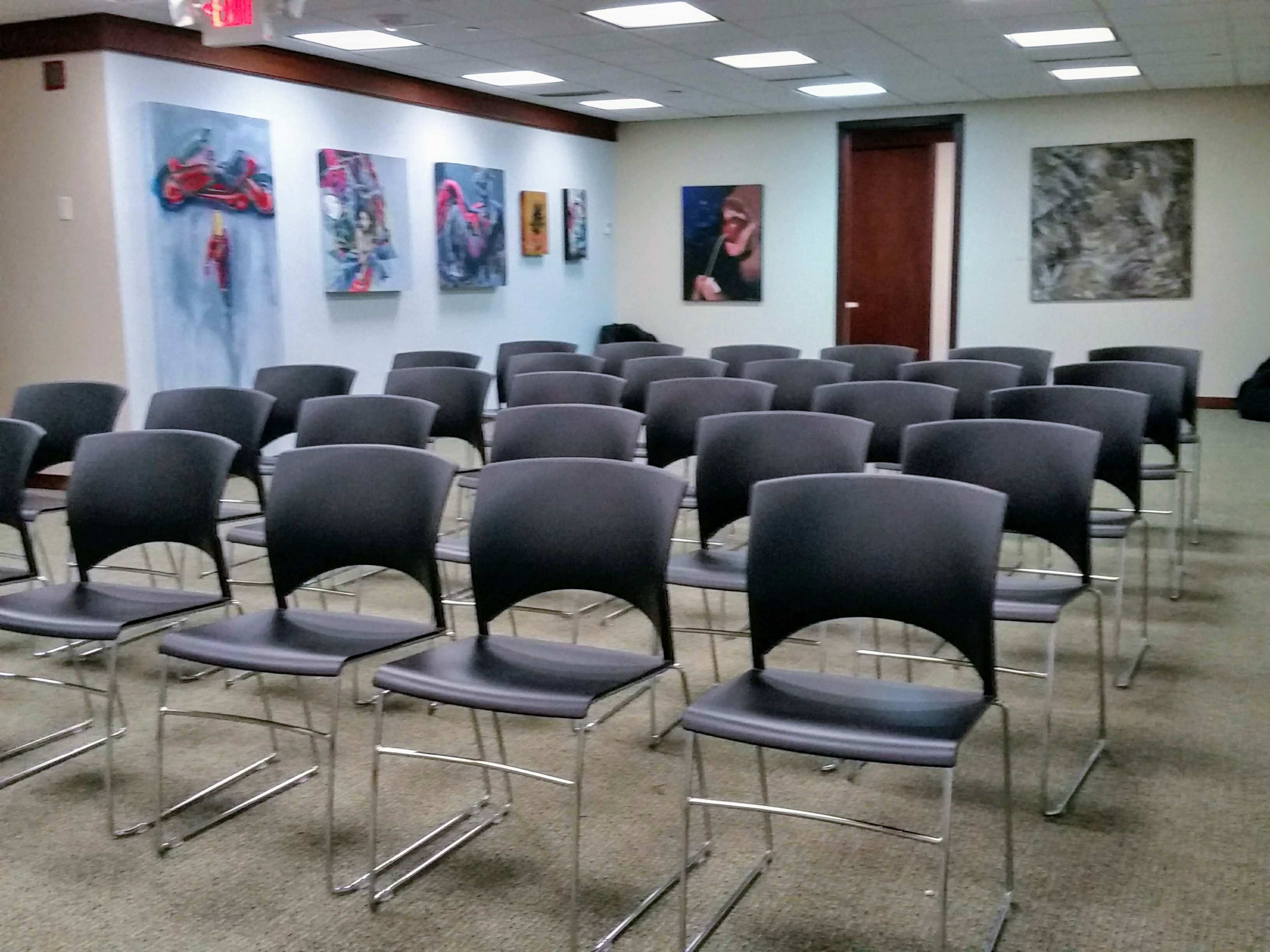 A row of gray chairs is arranged in a meeting room with colorful artwork displayed on the walls.