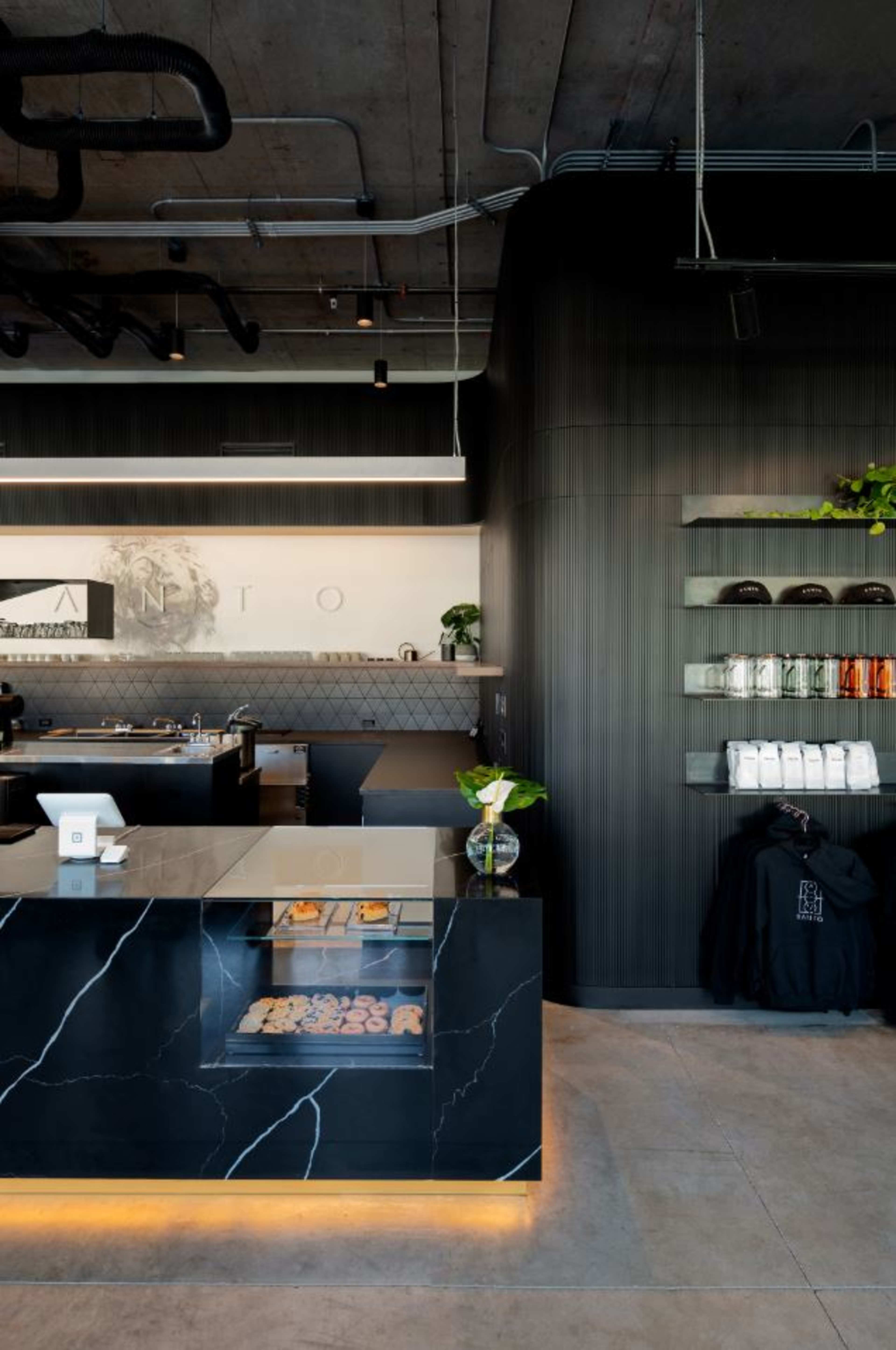 A modern café interior featuring a dark marble counter, a display case with pastries, and shelves stocked with various items against a minimalist backdrop.