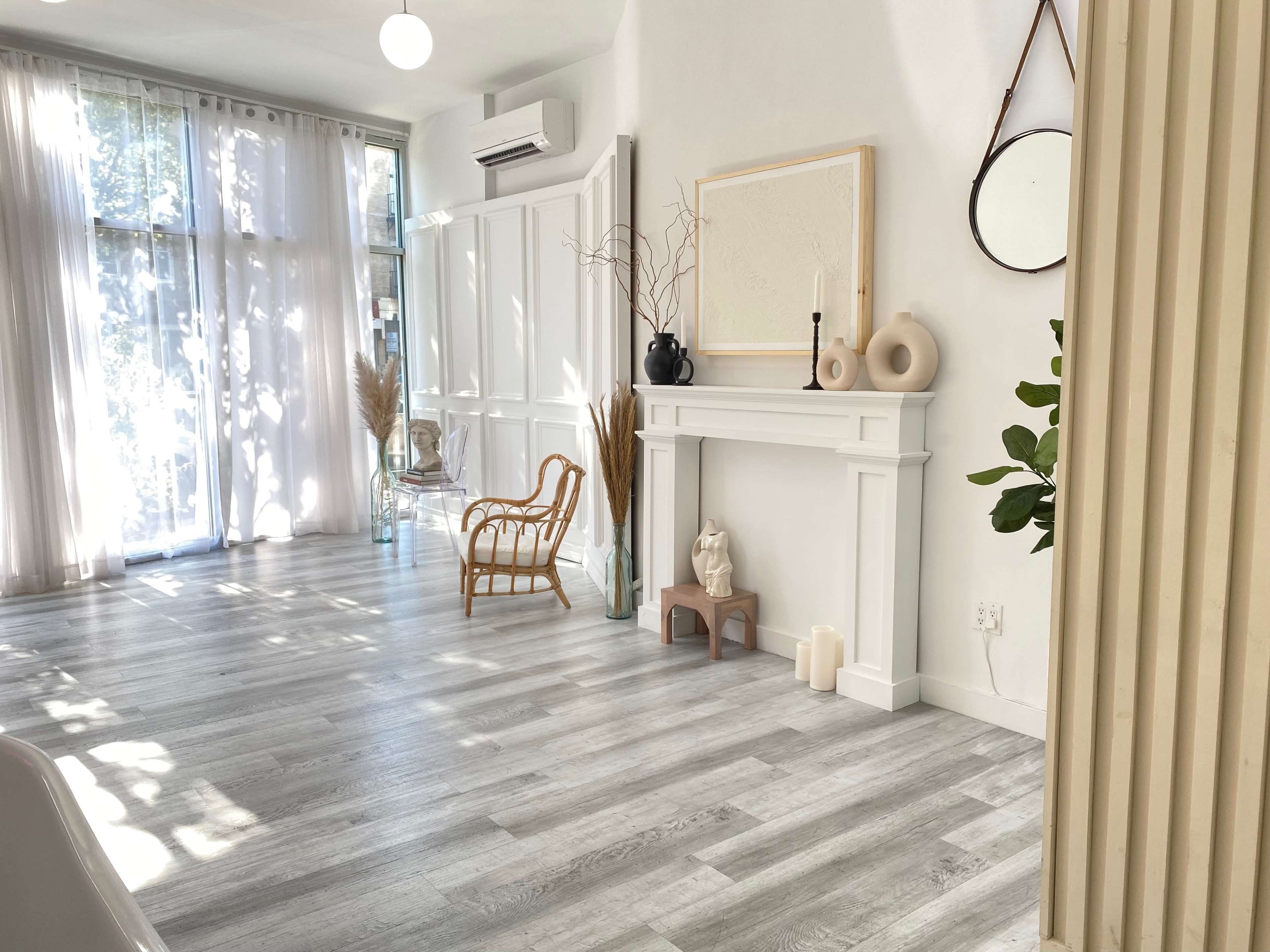 A bright, modern interior space featuring a fireplace, decorative items on a mantel, and natural light streaming through large windows.