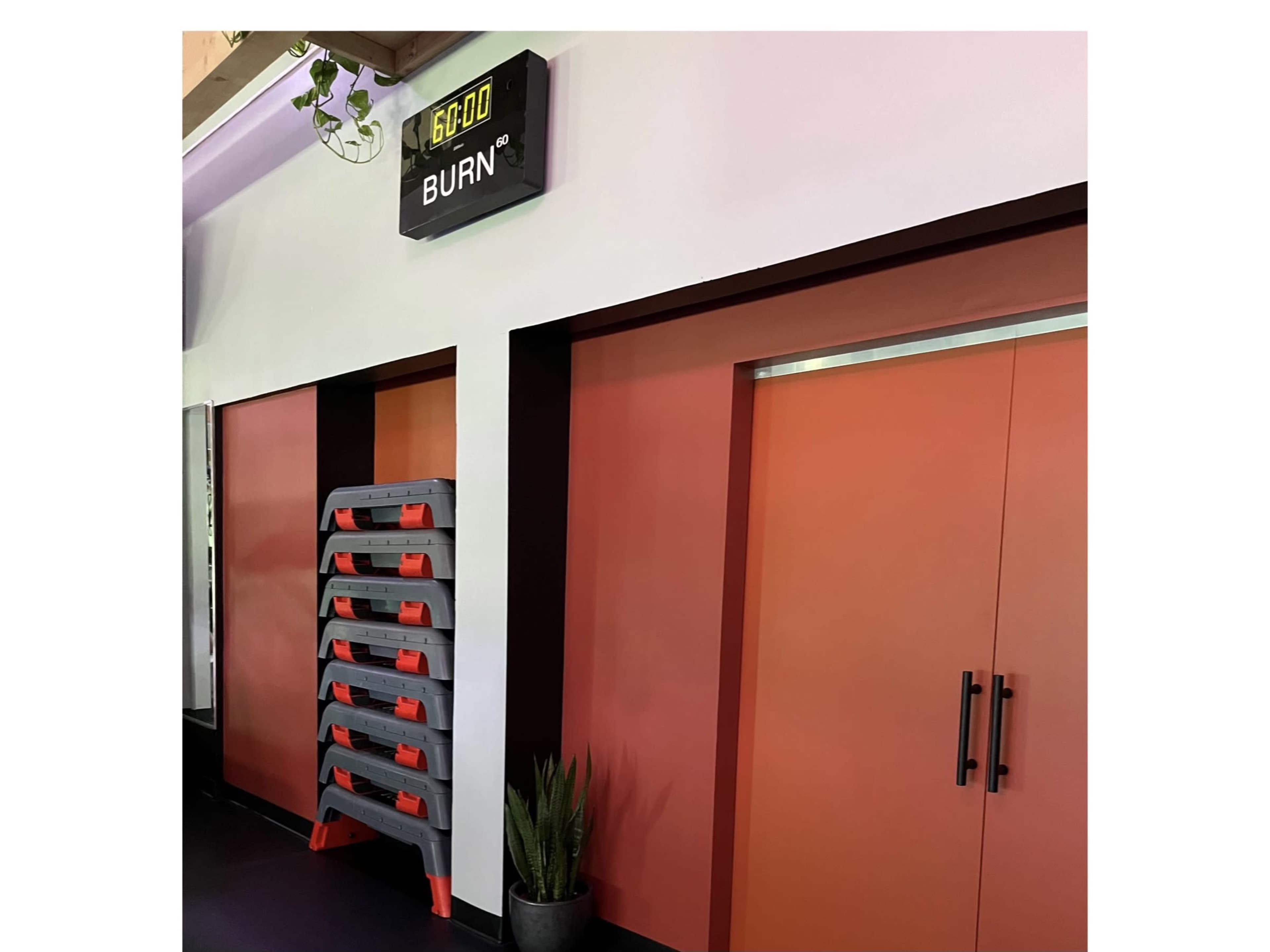 A fitness studio entrance with a digital display that reads "6,000" above a stacked exercise step platform and closed doors painted in a coral color.