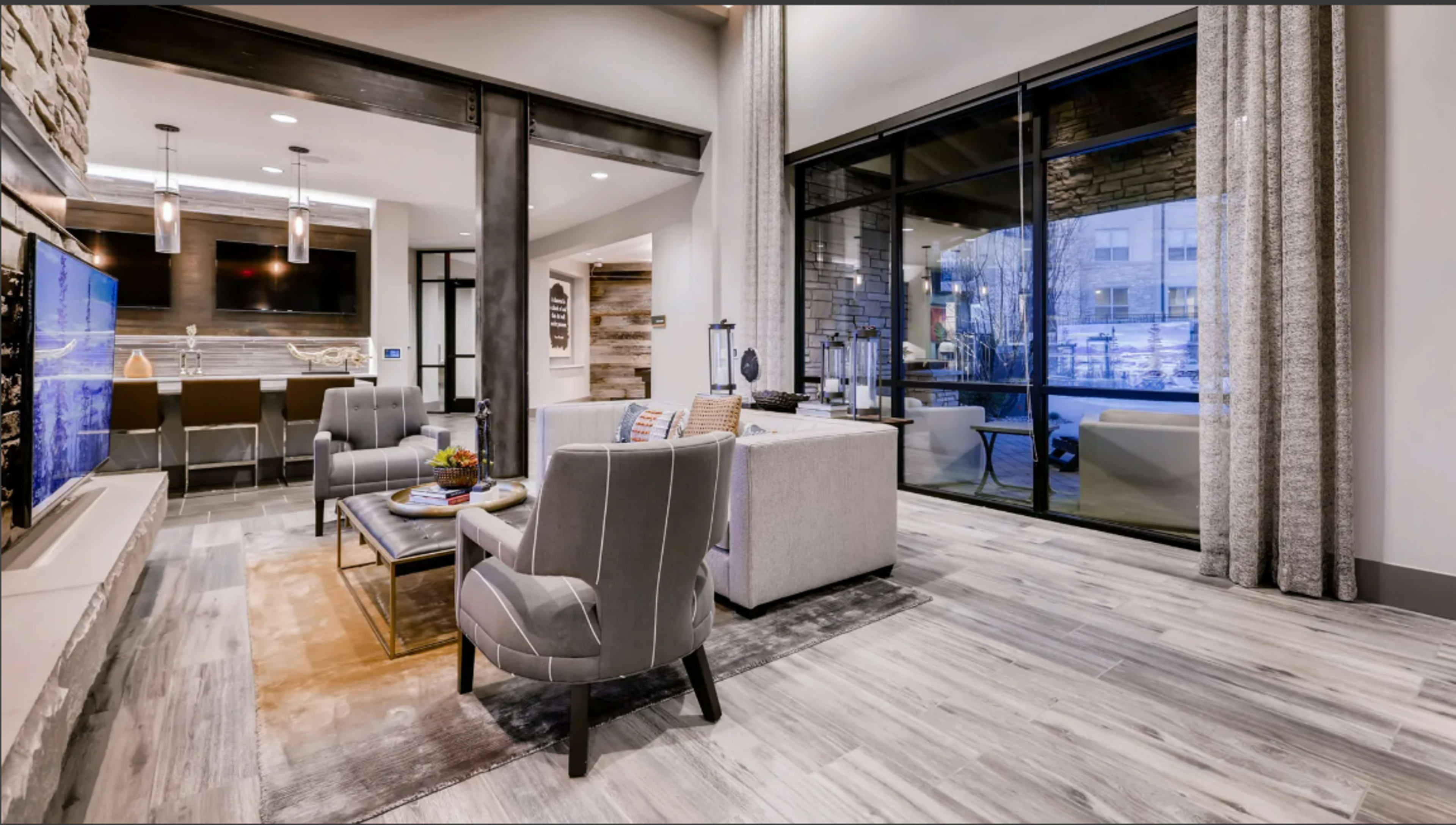 A modern living space with a seating area, a television mounted on the wall, and large windows overlooking an outdoor view.