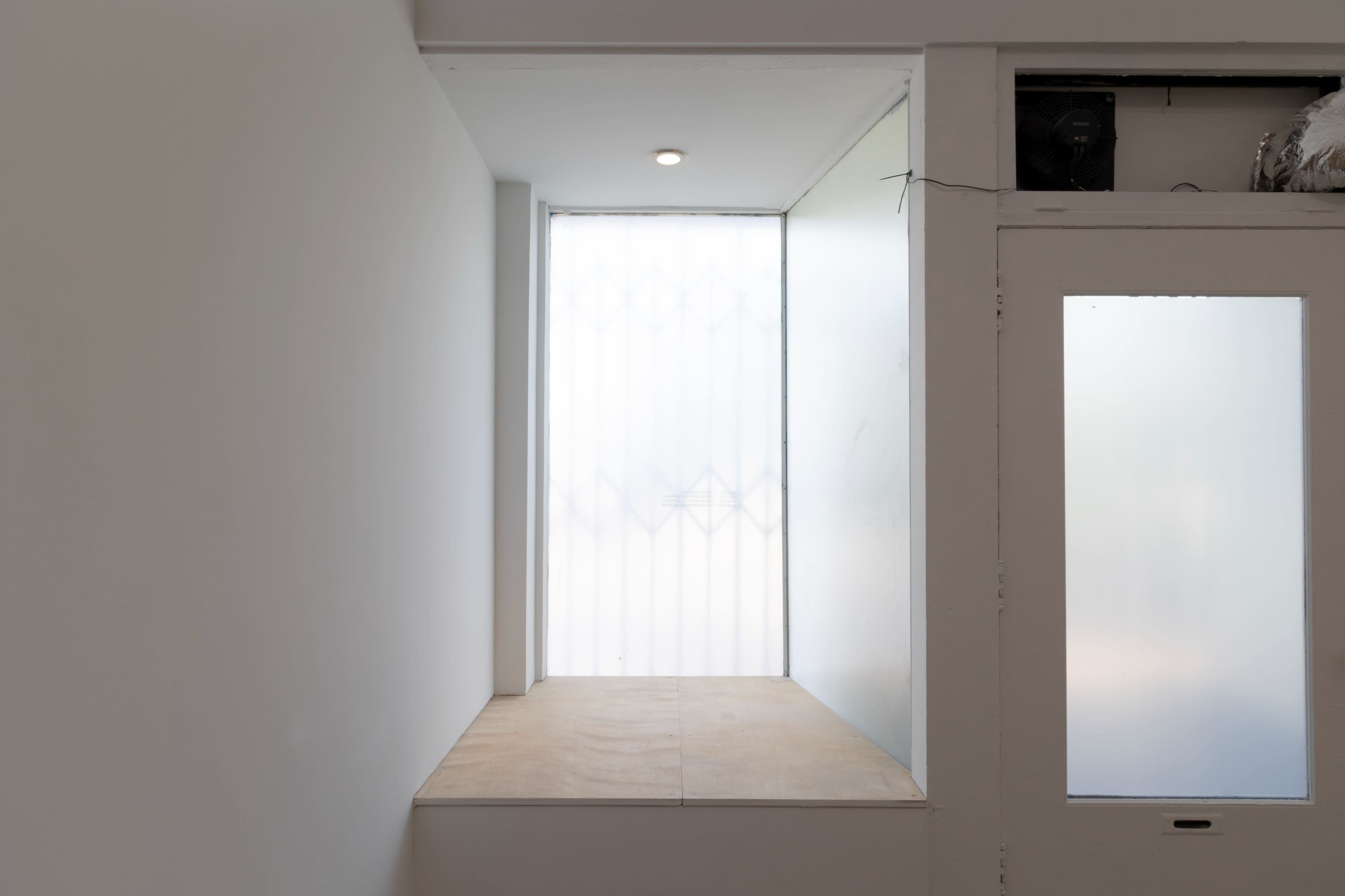 A small, empty nook with a wooden ledge and a frosted glass window next to a door with a glass panel.