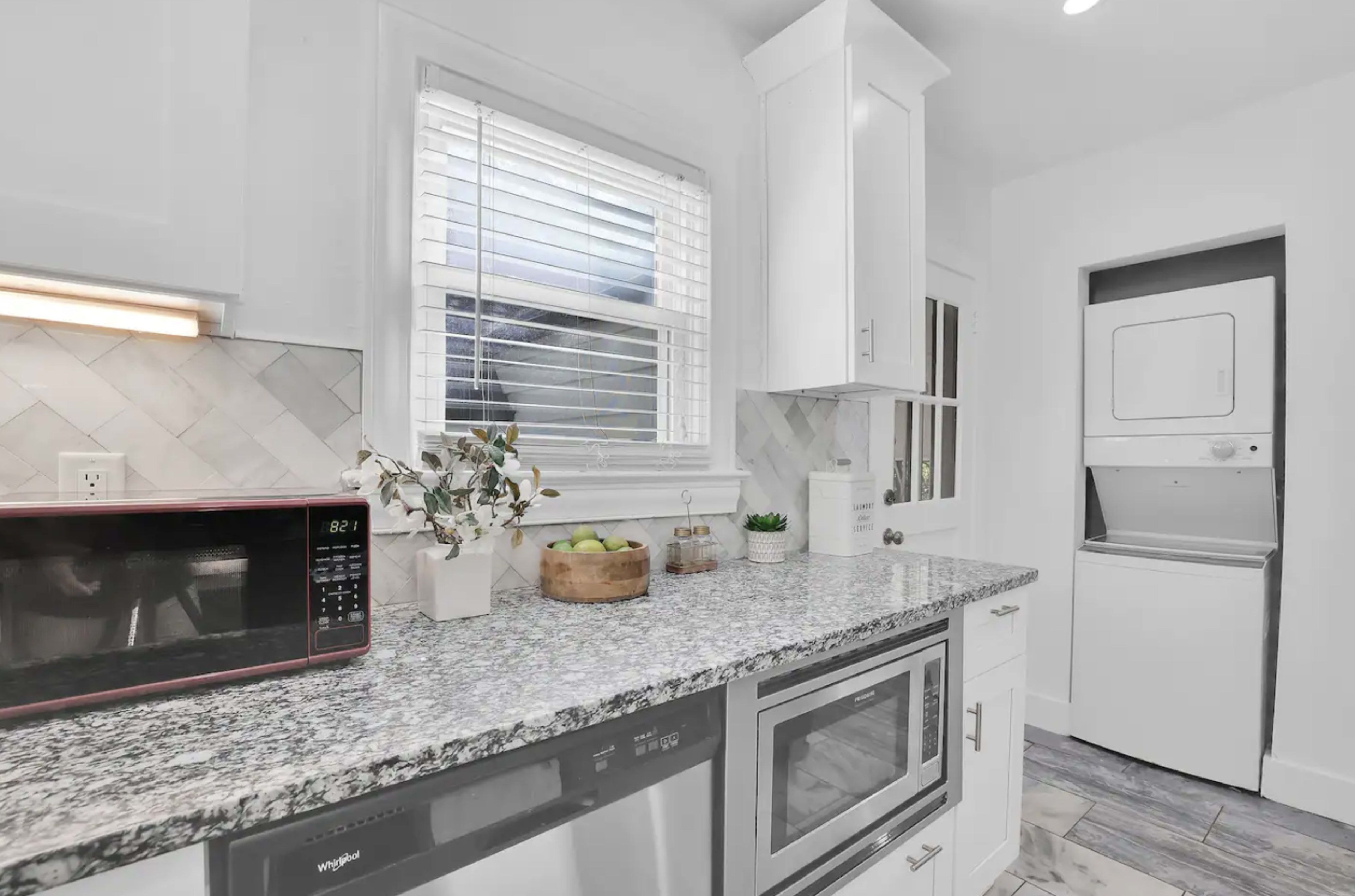 A modern kitchen features gray granite countertops, a microwave, an oven, and a stacked washer and dryer in a utility space.