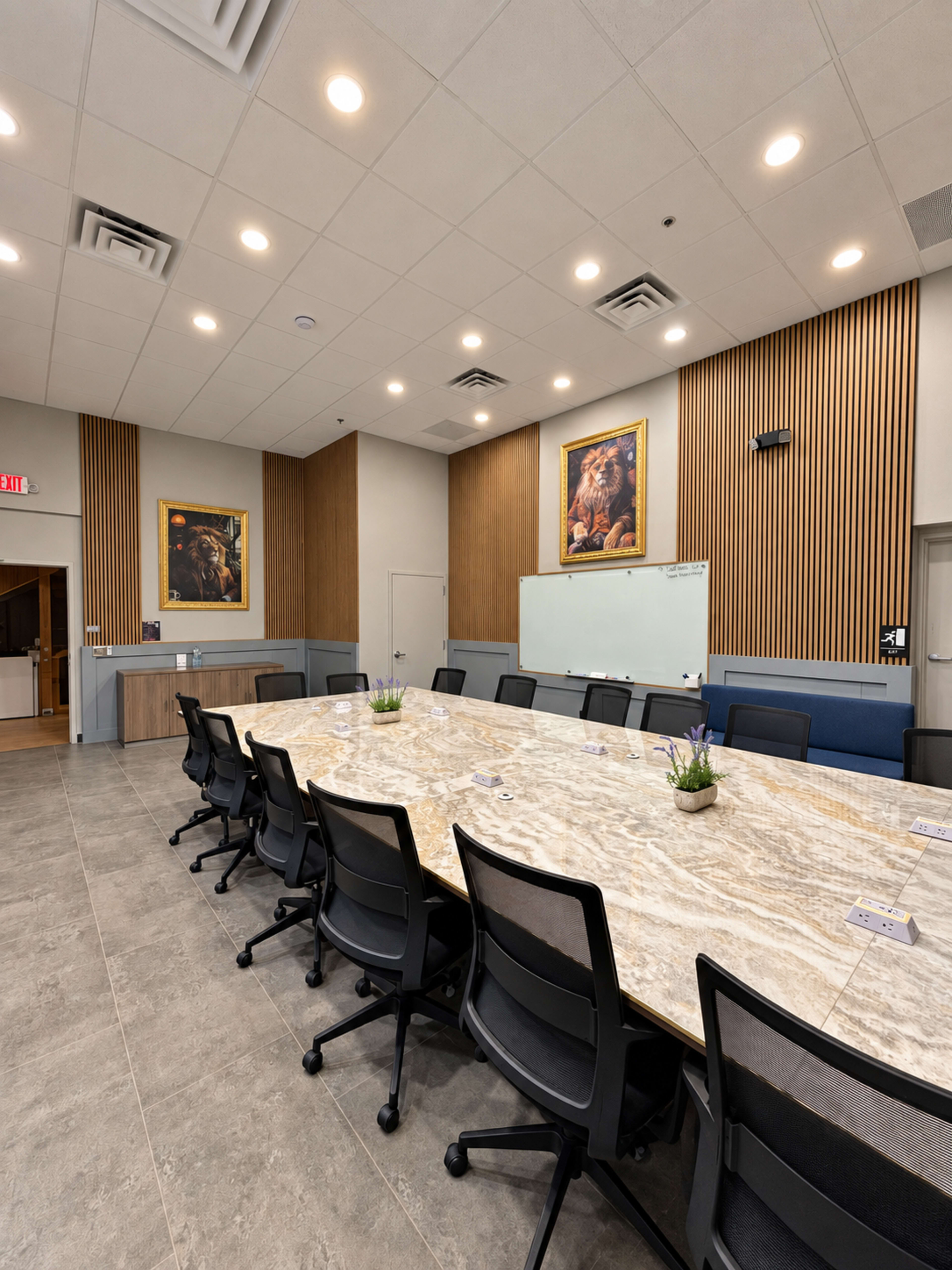A large conference room features a long marble table surrounded by black chairs, with two framed artworks on the walls and a whiteboard at one end.