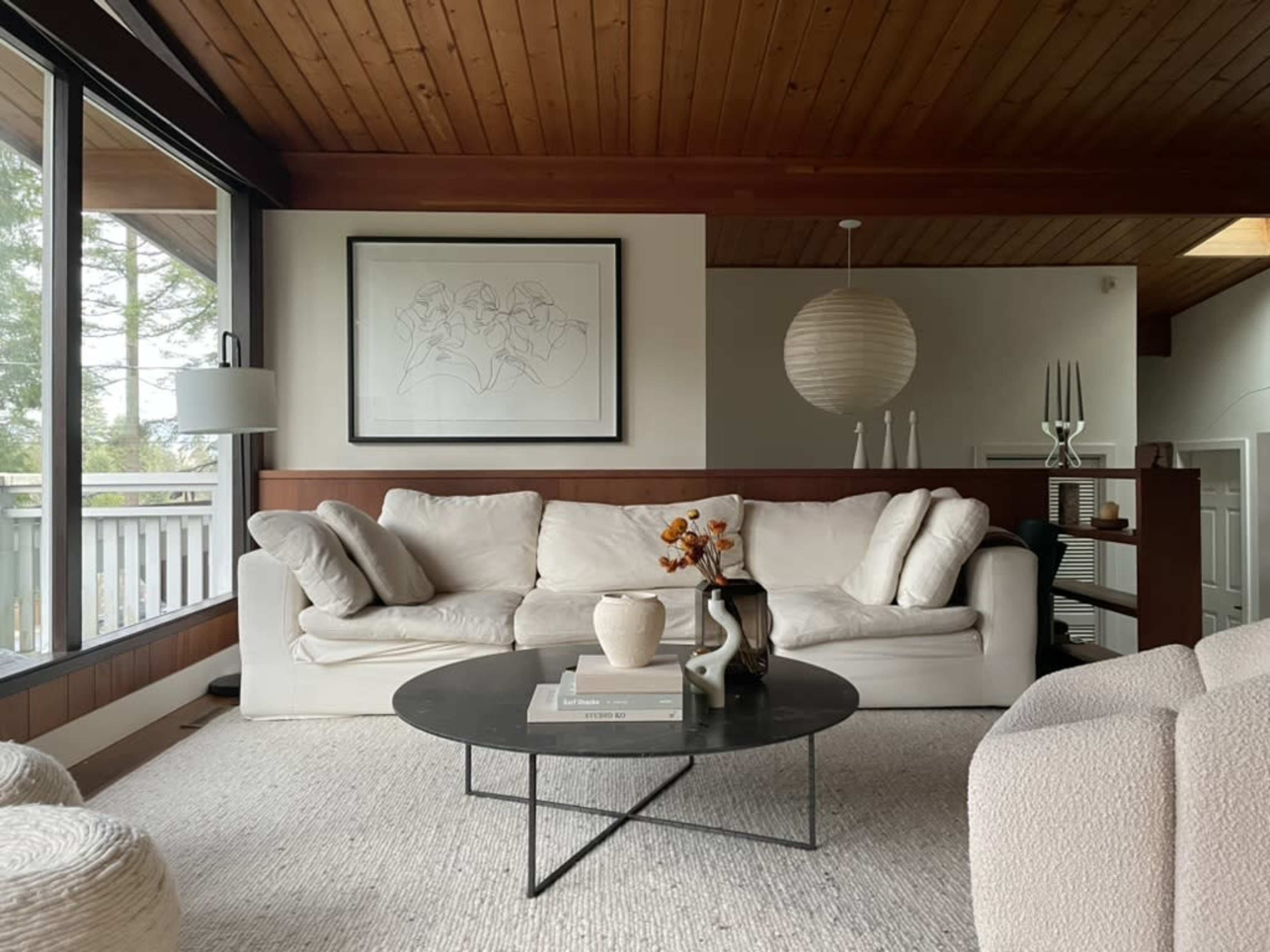 The image shows a modern living room with a white sofa, a round black coffee table, and large windows that let in natural light.