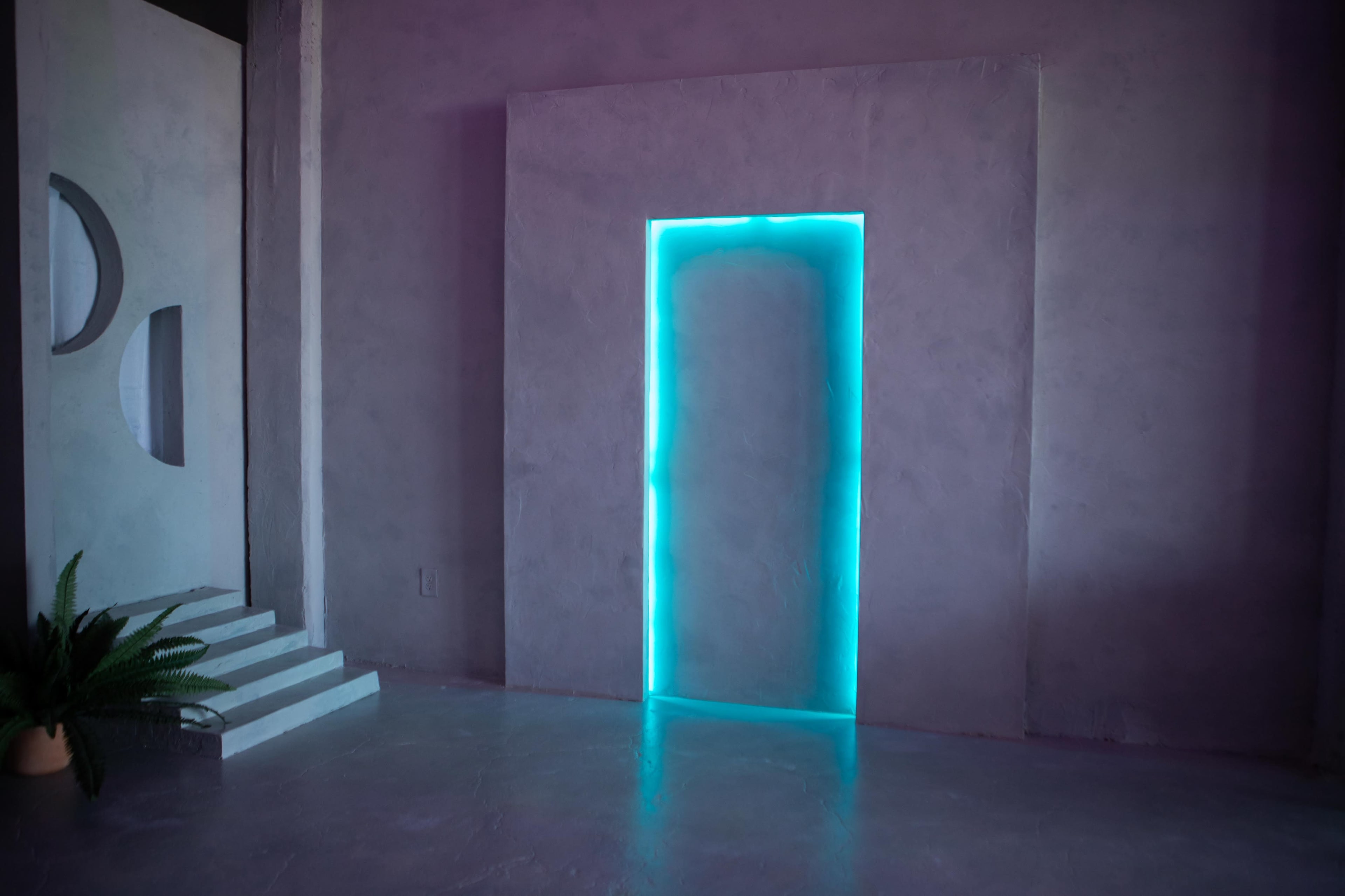 The image shows a modern interior with a textured wall, featuring a glowing turquoise doorway and a set of steps leading to a minimalist design element on the left.