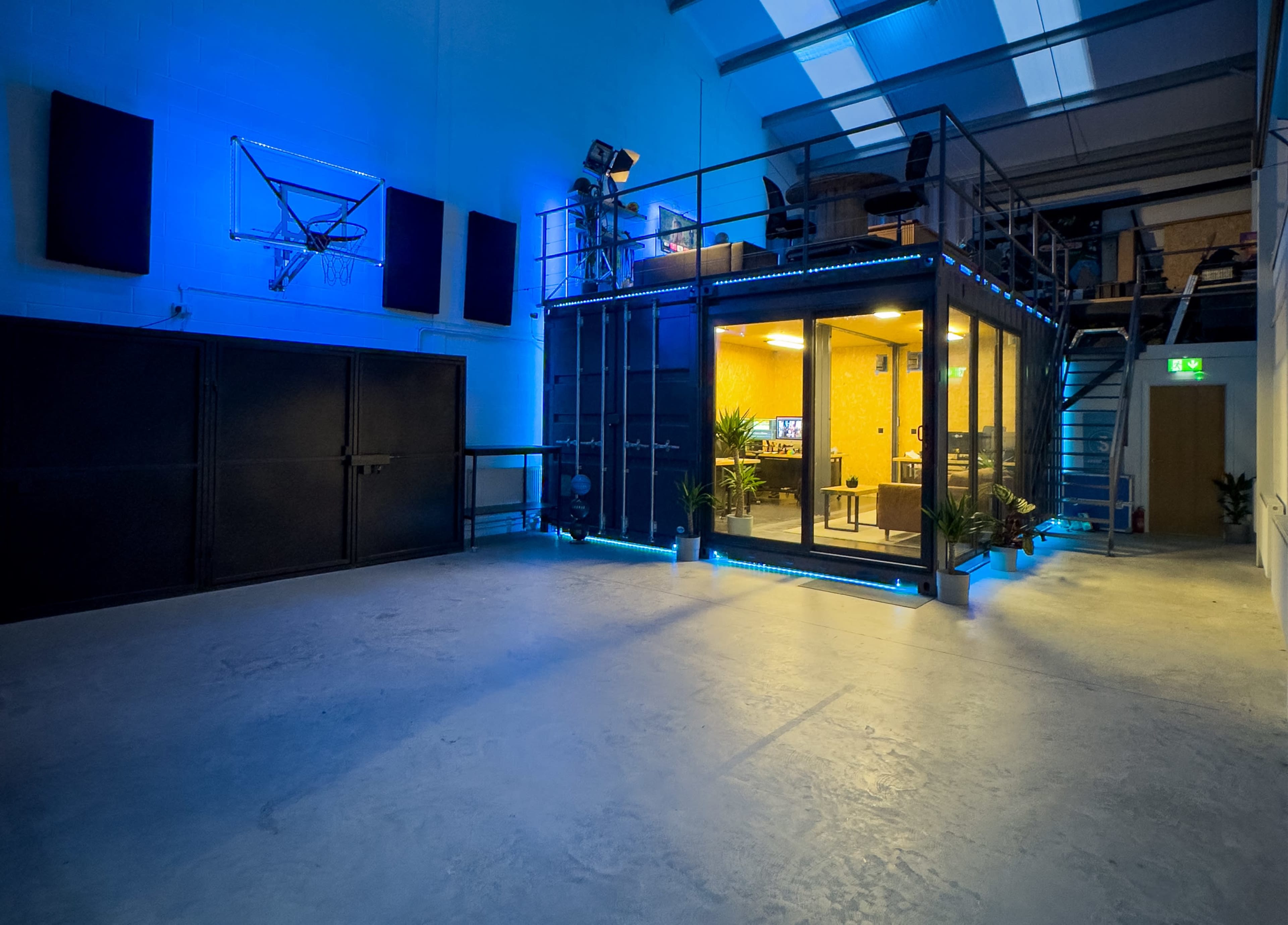 A modern, open commercial space with a glass-walled office area and a basketball hoop mounted on the wall.