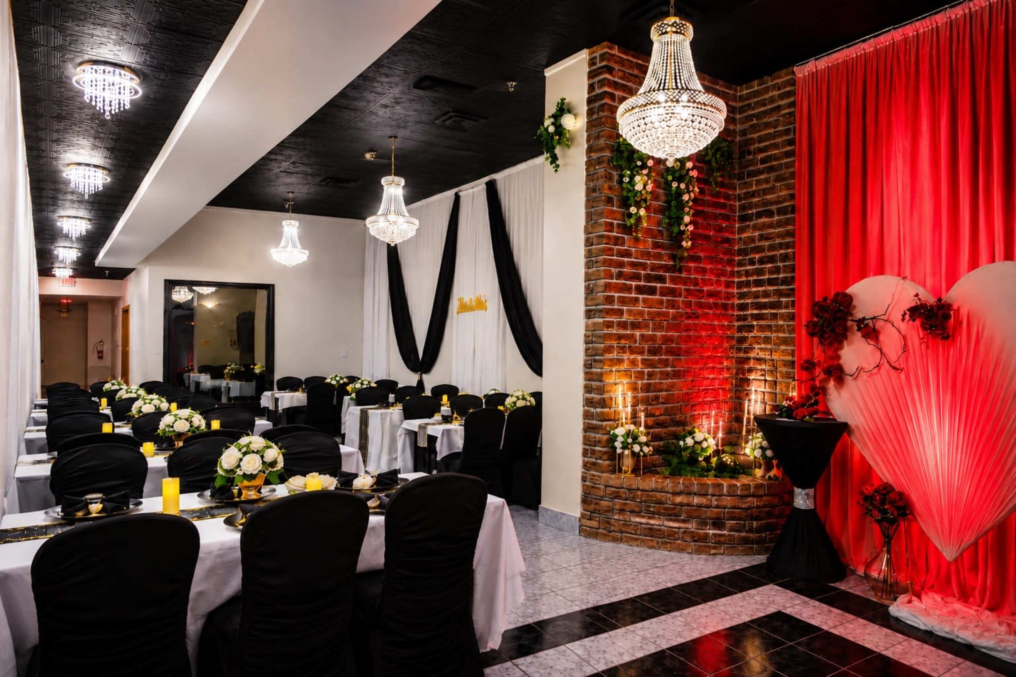 The image shows a elegantly decorated banquet hall with tables set for a formal event, featuring black chairs and white tablecloths, along with floral centerpieces.