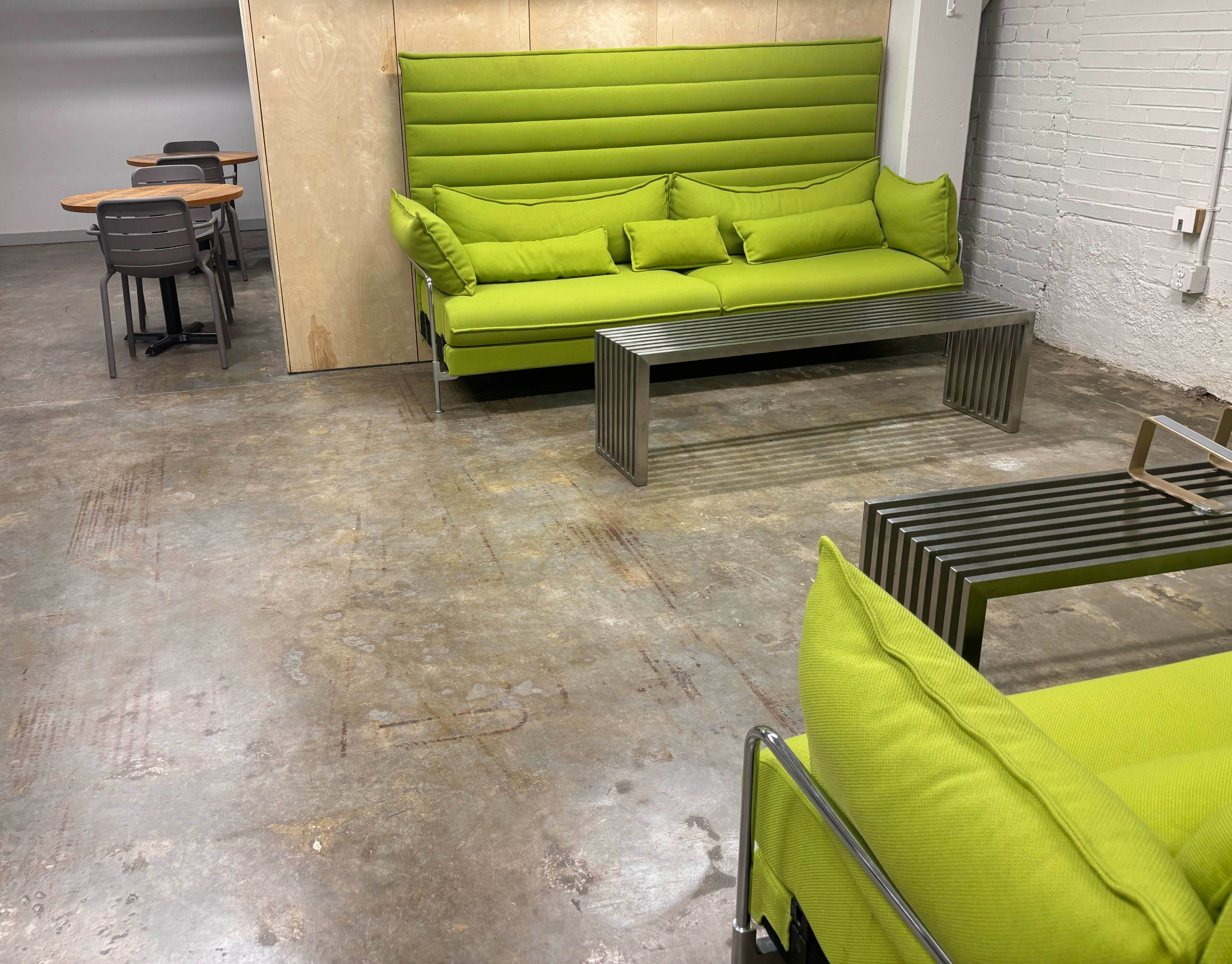 The image shows a modern seating area with bright green sofas and a metal coffee table, along with a small dining table and chairs in the background.