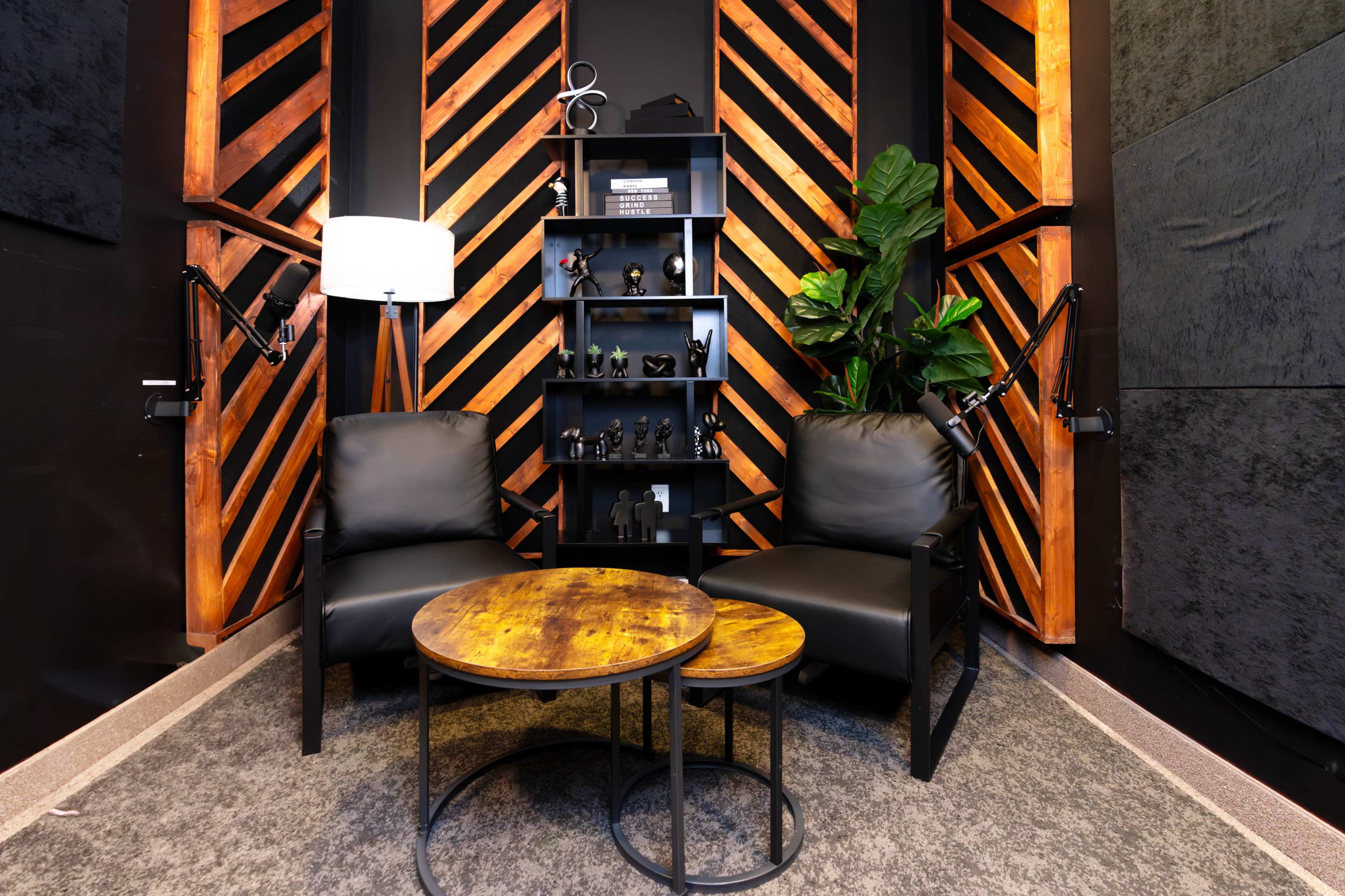 A cozy seating area featuring two black chairs and a wooden coffee table against a backdrop of striped wooden paneling and a wall shelf with decorative items.