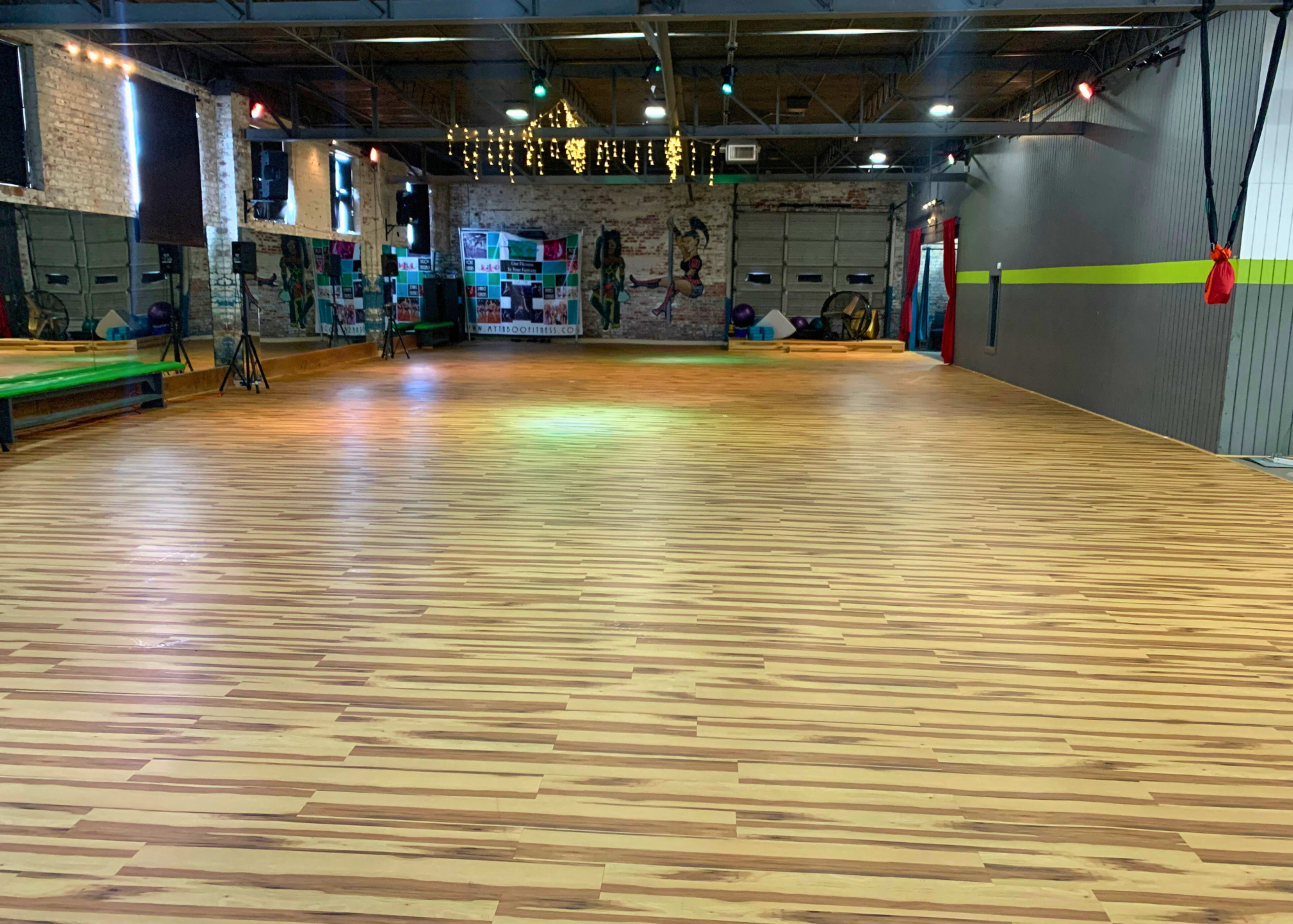 A spacious dance studio with a wooden floor, bright lights, and a mirrored wall.