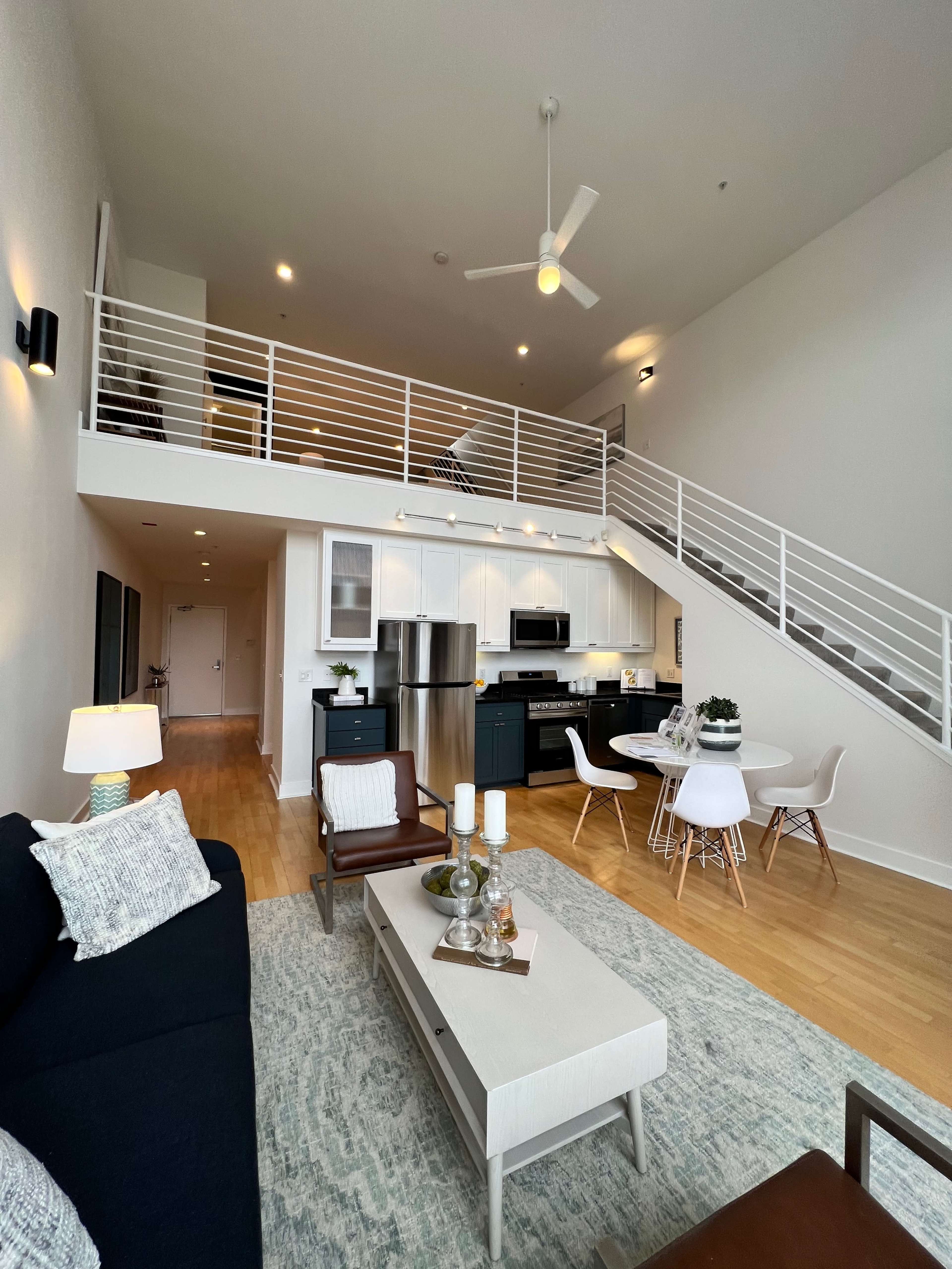 A modern, two-level apartment interior featuring a living area with a sofa, coffee table, and dining space, along with a staircase leading to an upper level.